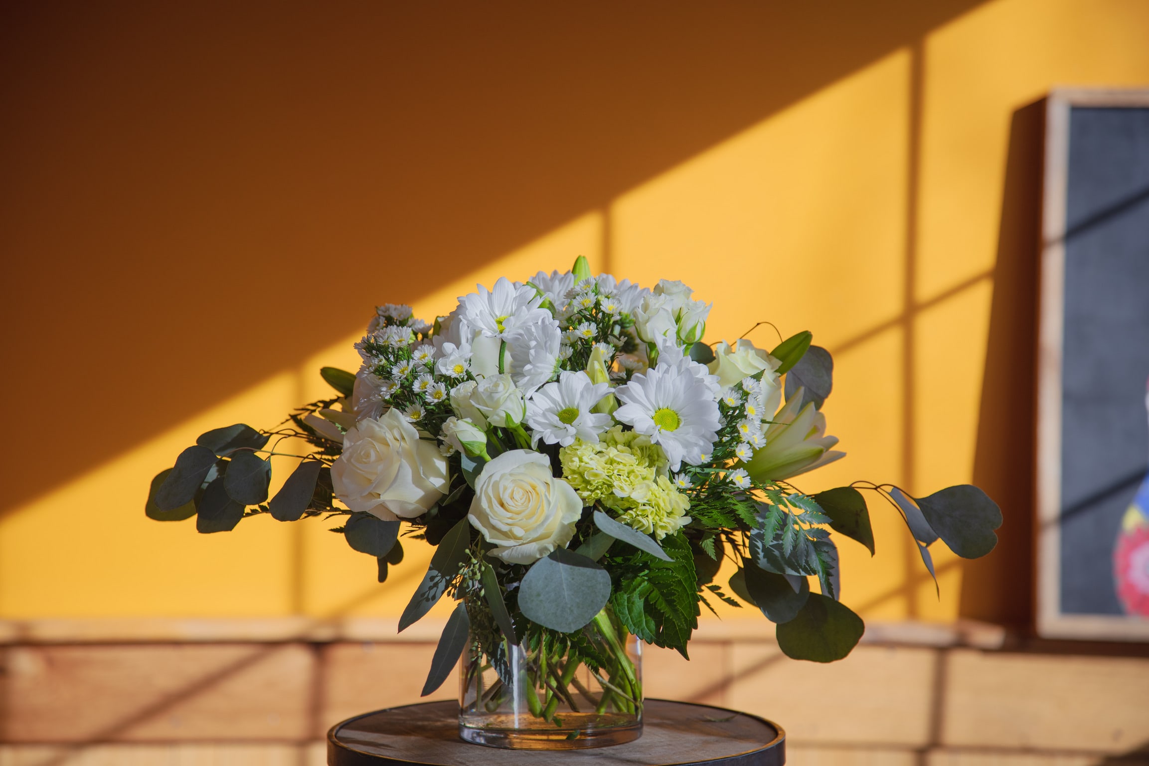White flowers in a clear glass vase with dark foliage