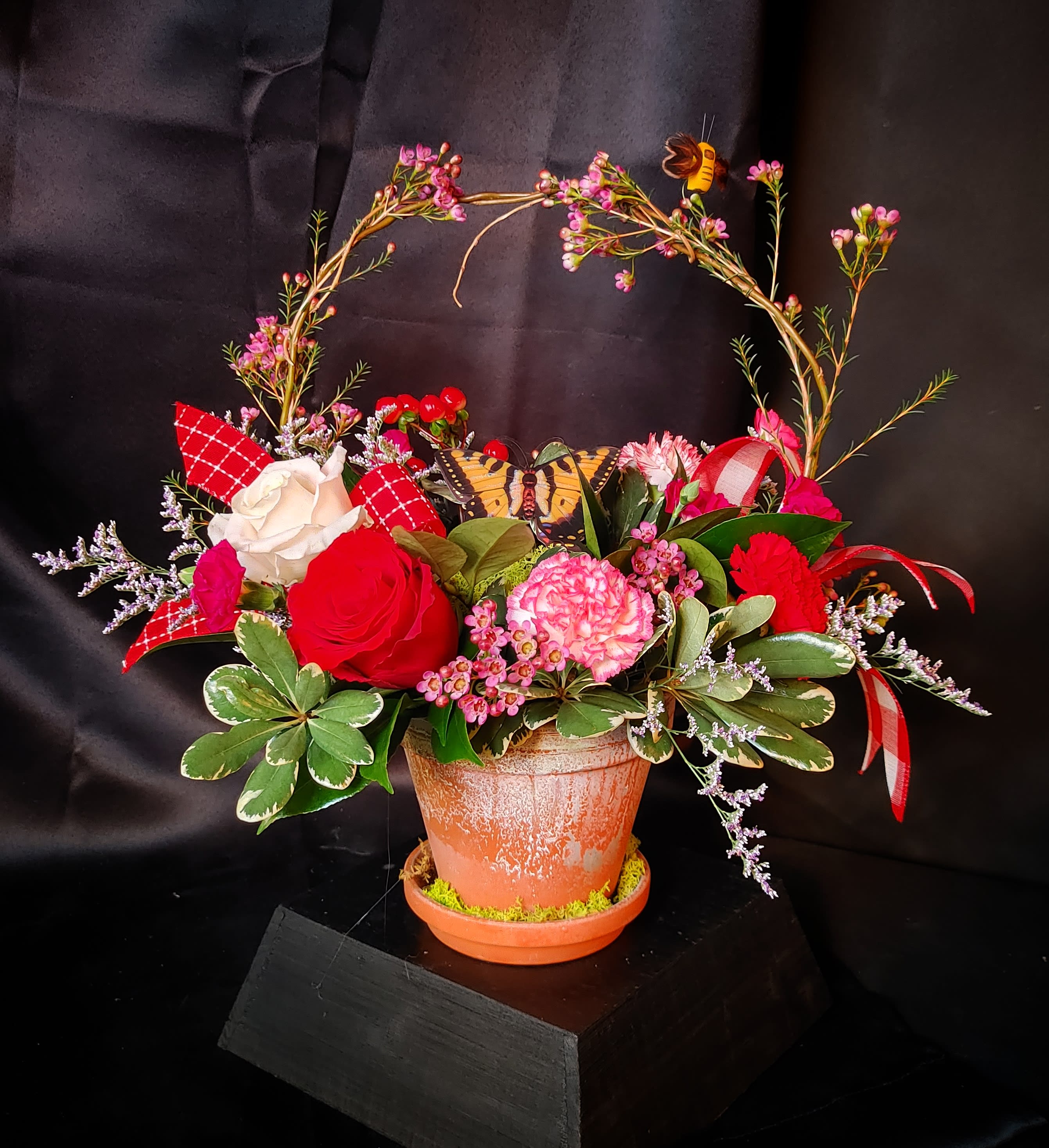 Mixed pink and red floral arrangement in a terracotta pot with a butterfly decoration