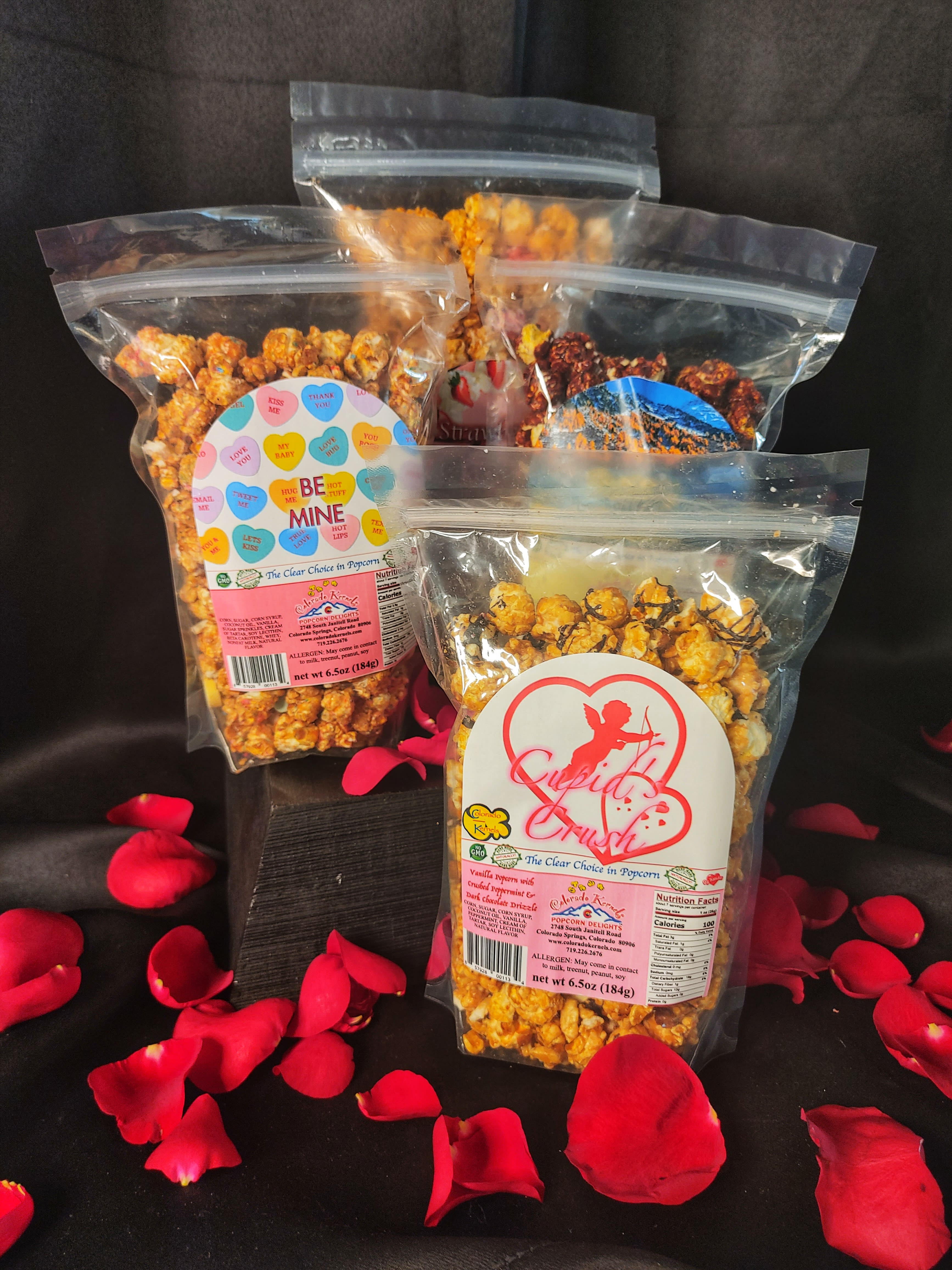 Three bags of flavored popcorn with rose petals scattered around them