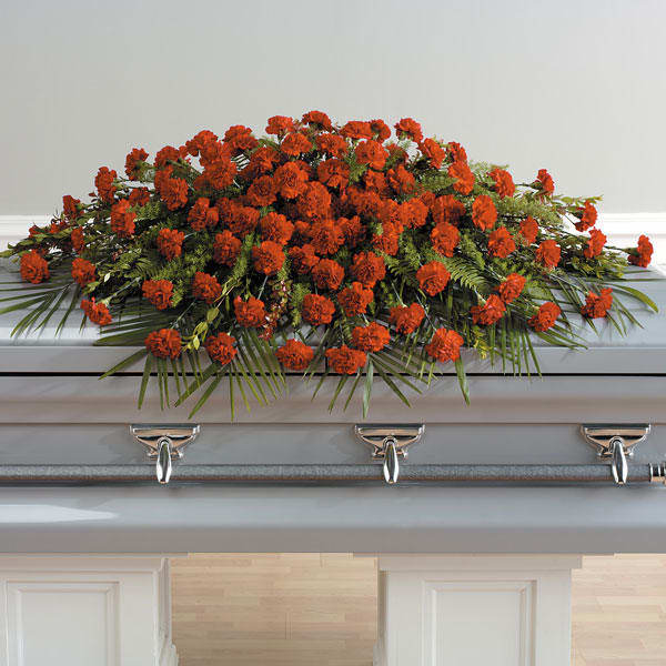 Orange floral casket spray with greenery on a white coffin