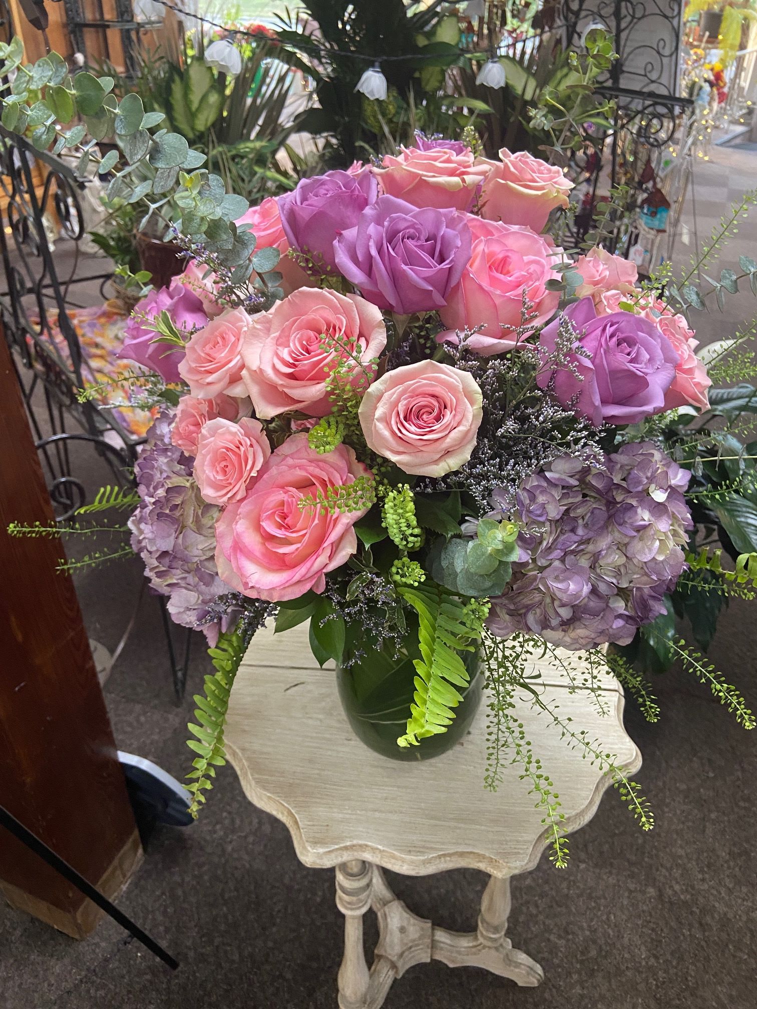 Arrangement of pink and lavender roses with purple hydrangeas in a green glass vase on a small table