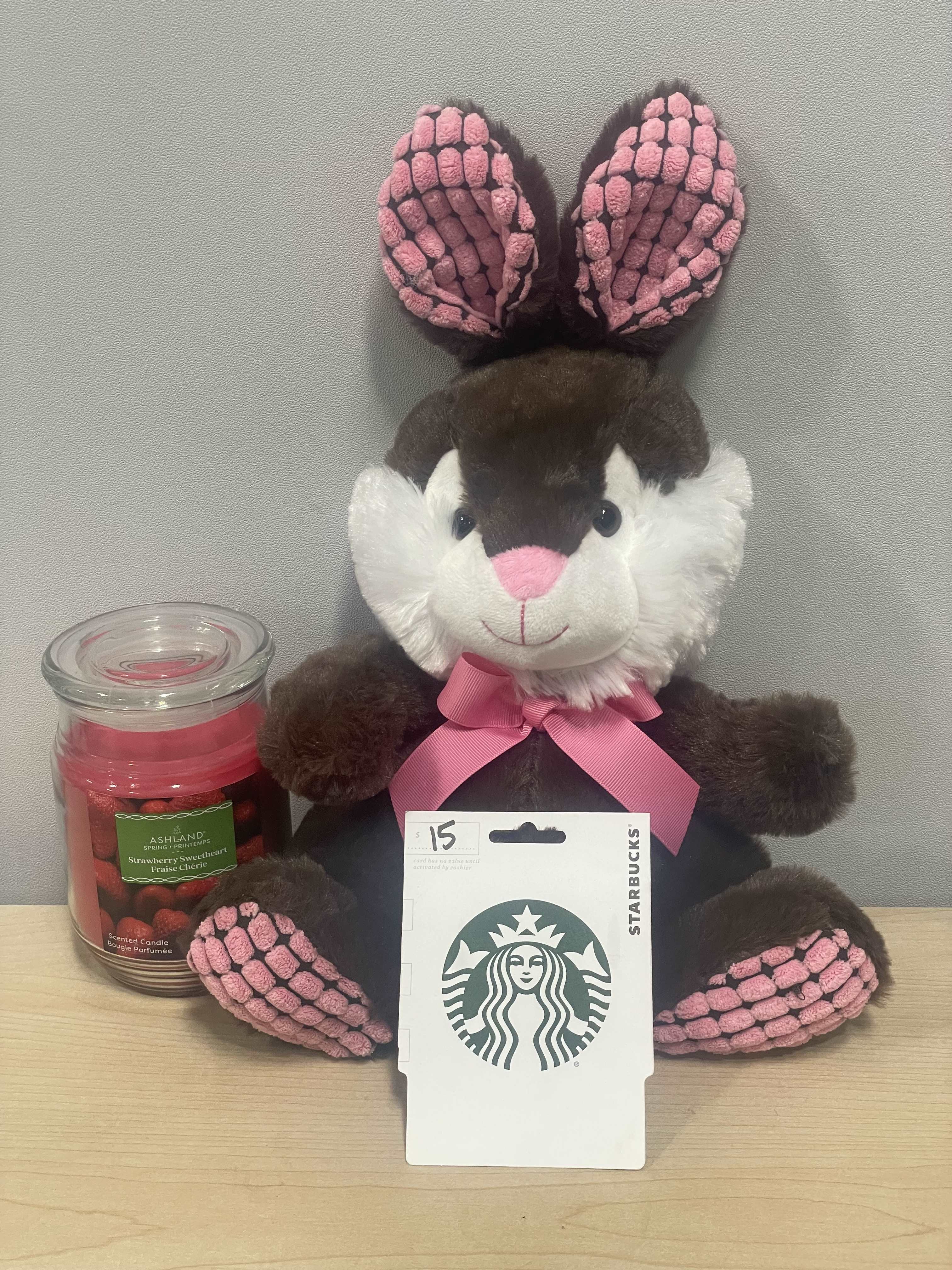 Plush bunny with a pink ribbon beside a candle and Starbucks gift card
