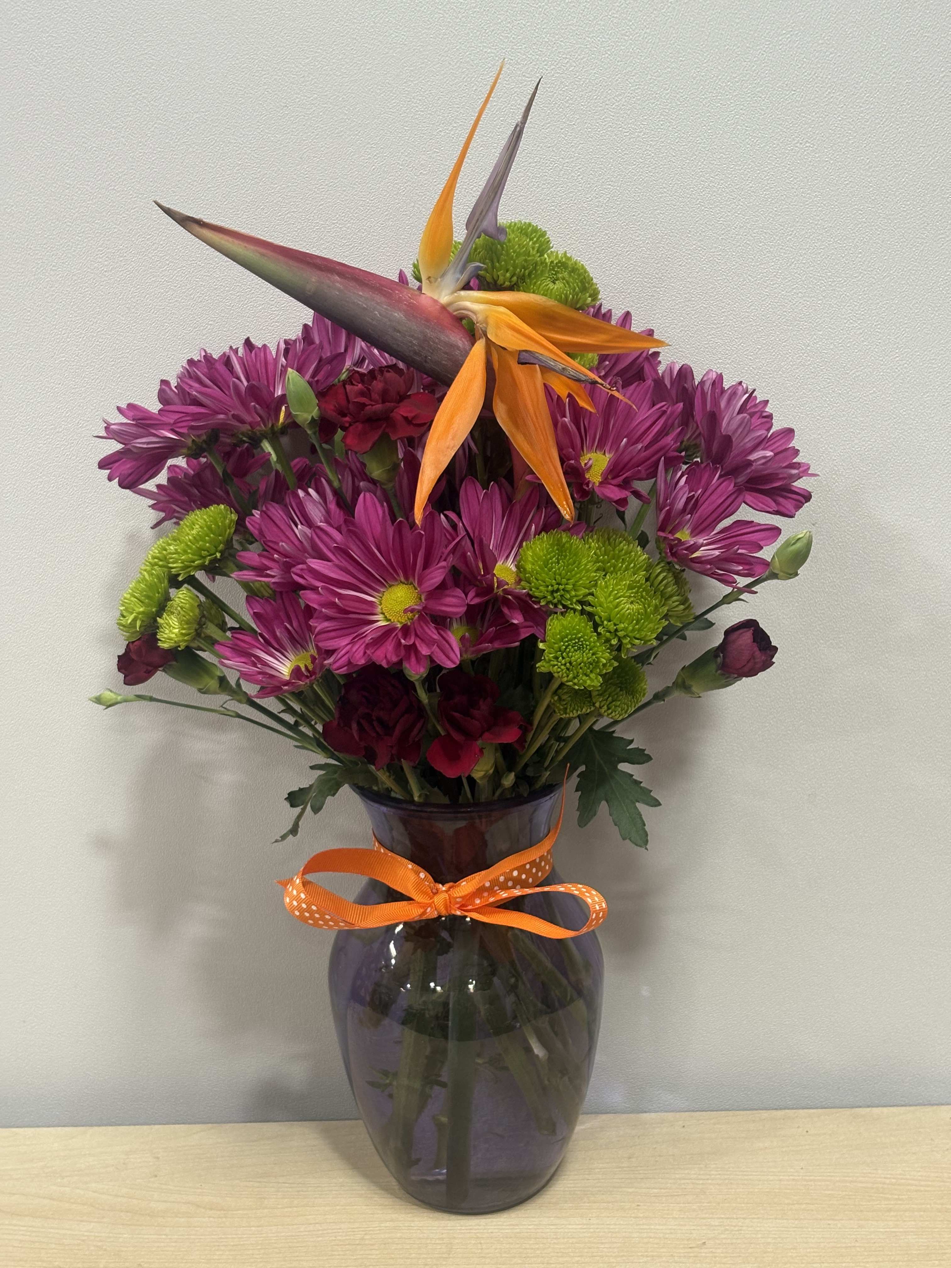 Purple and green bouquet with orange bird-of-paradise in a glass vase