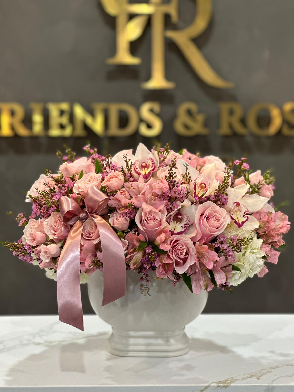 Pink roses and orchids arranged in a white vase with a satin ribbon