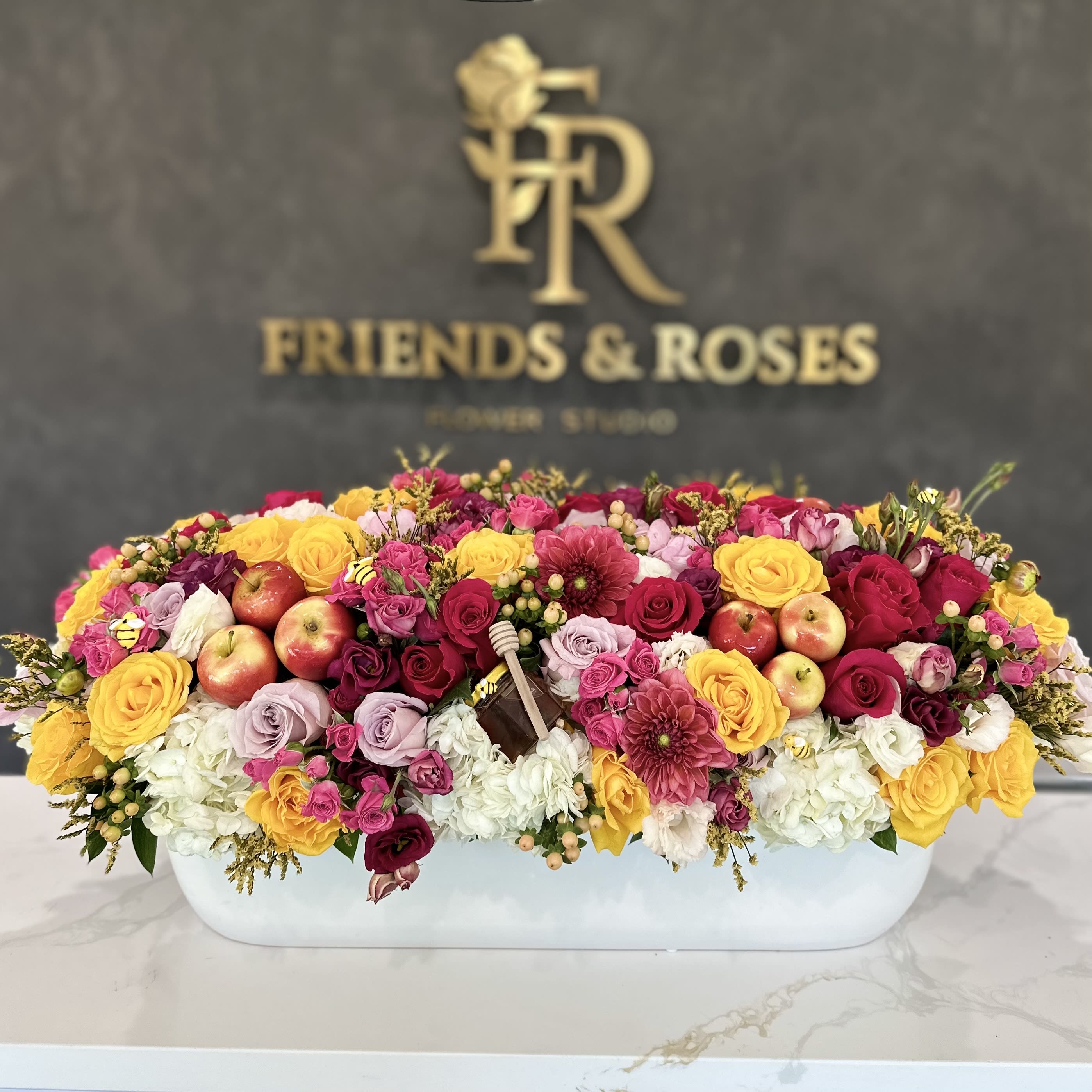 Large mixed flower arrangement in a white rectangular container with apples
