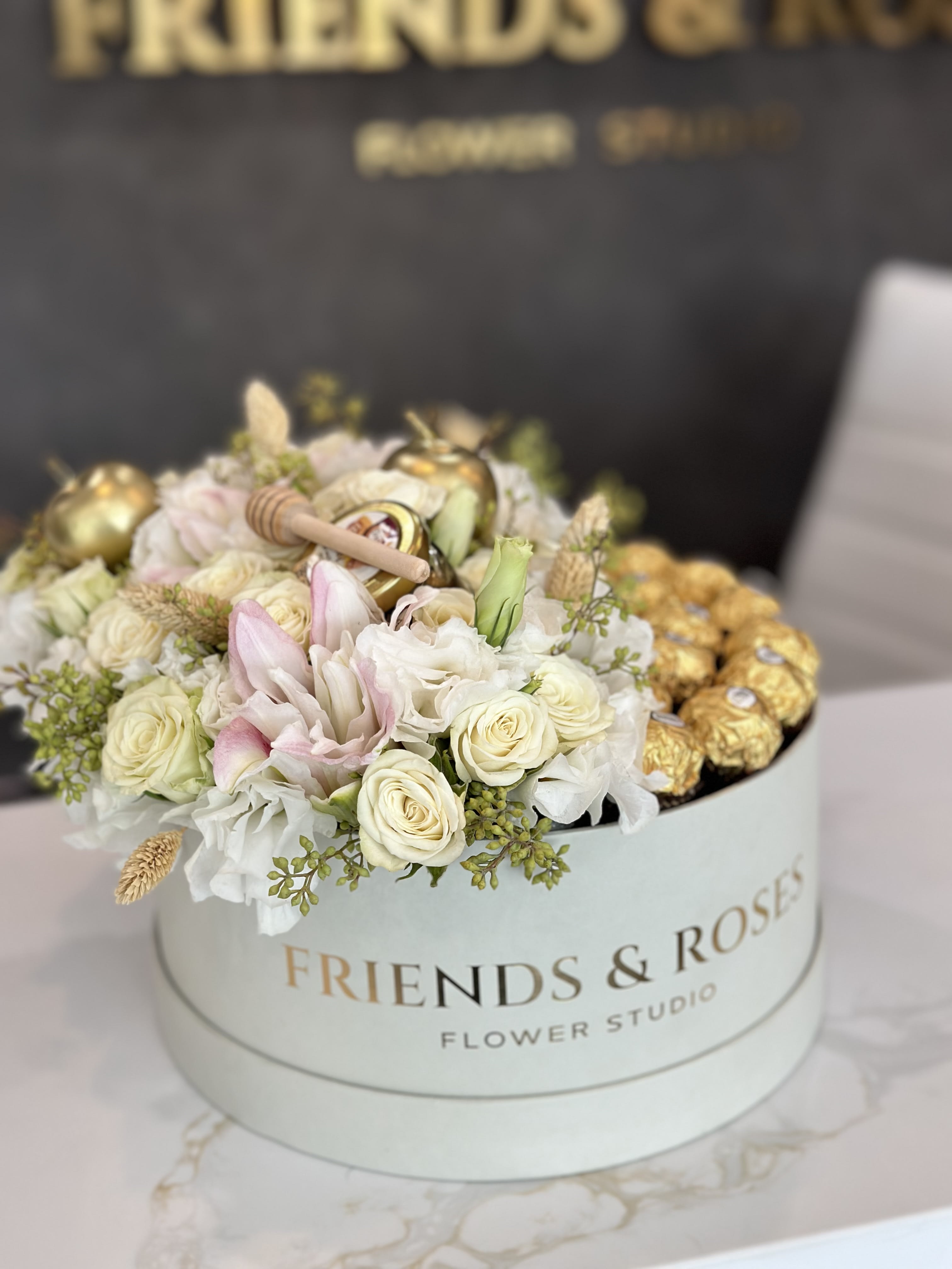 Round box of white and blush roses with gold chocolates on top