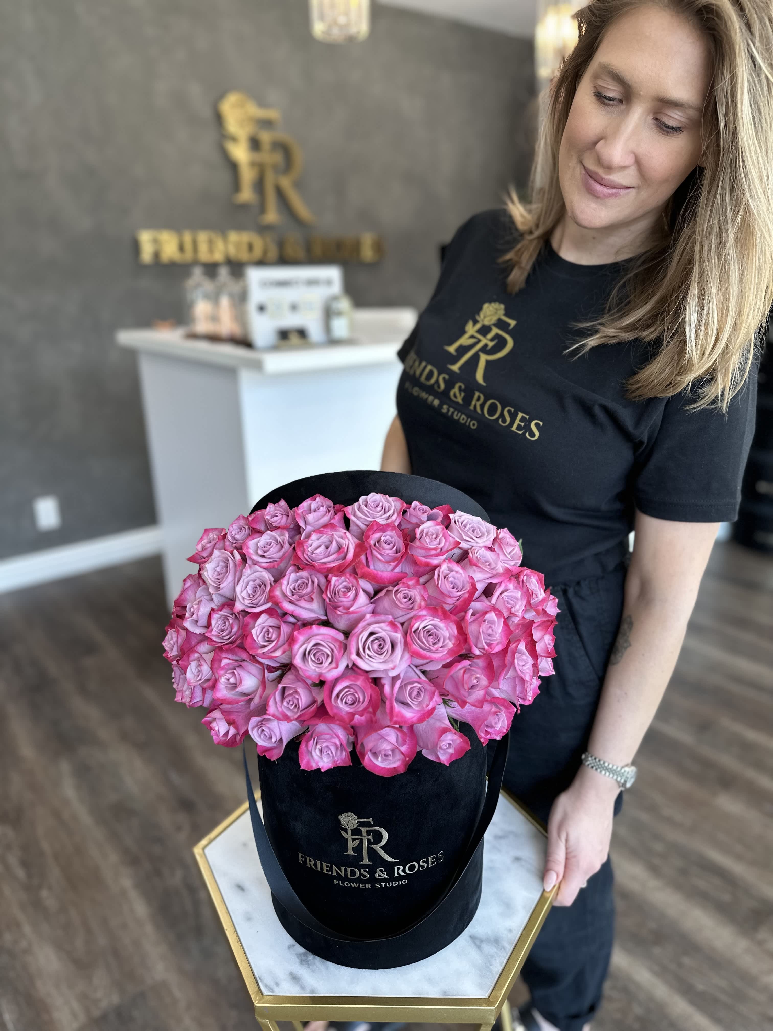 Pink roses arranged in a black hatbox held by a woman