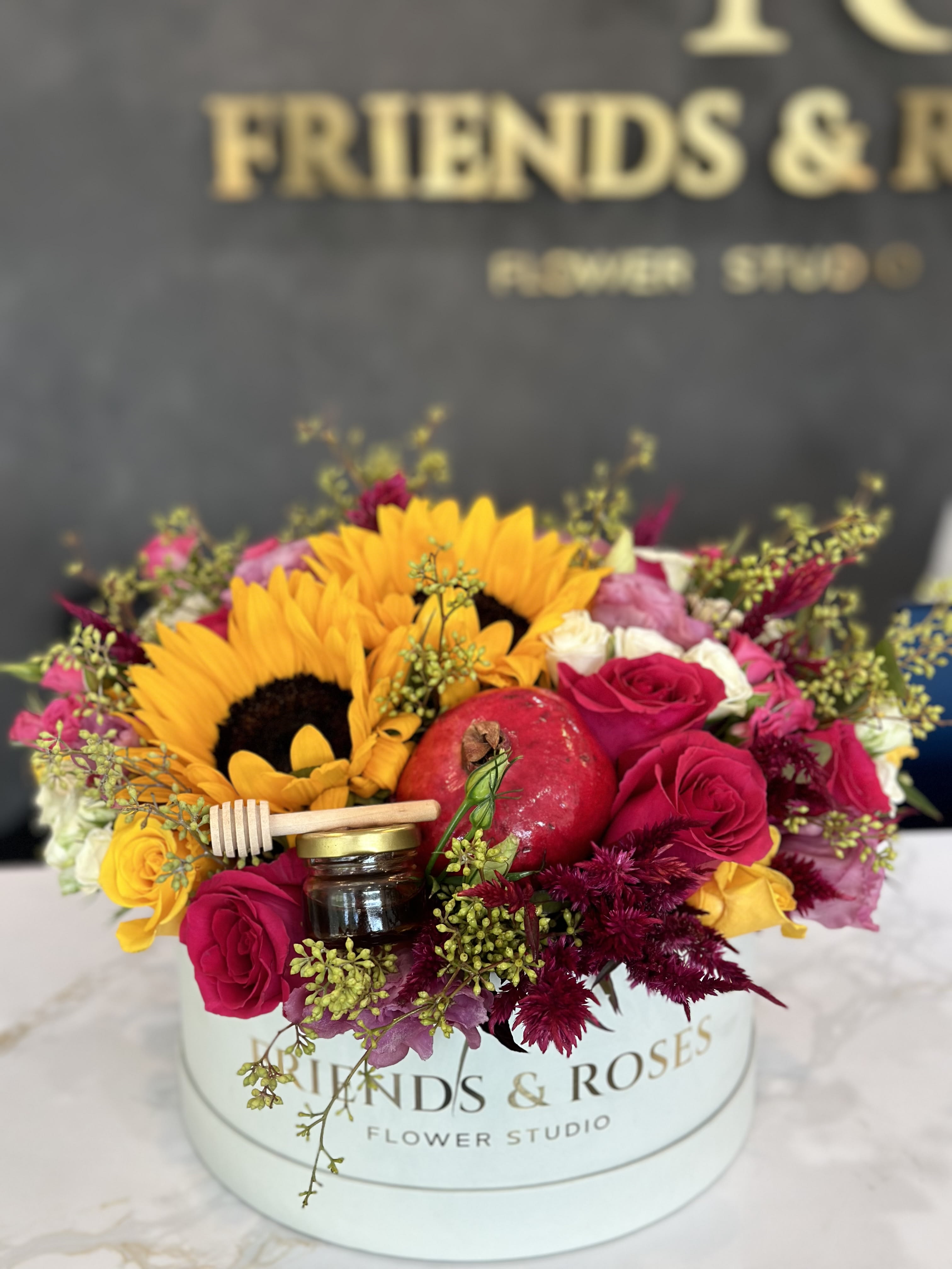 Bouquet with sunflowers, red roses, and a pomegranate in a round box