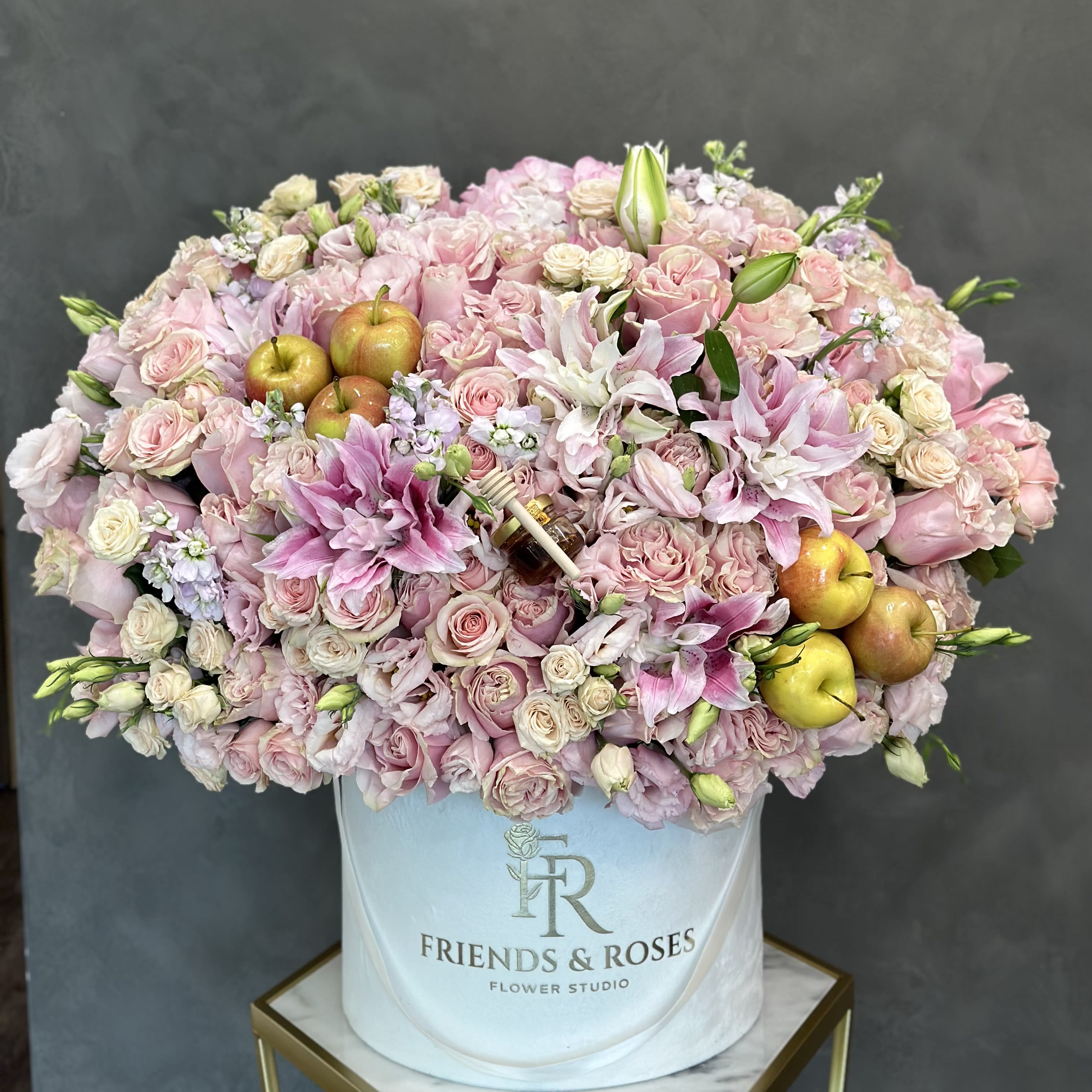 Large pink rose and lily arrangement in a white hat box with apples