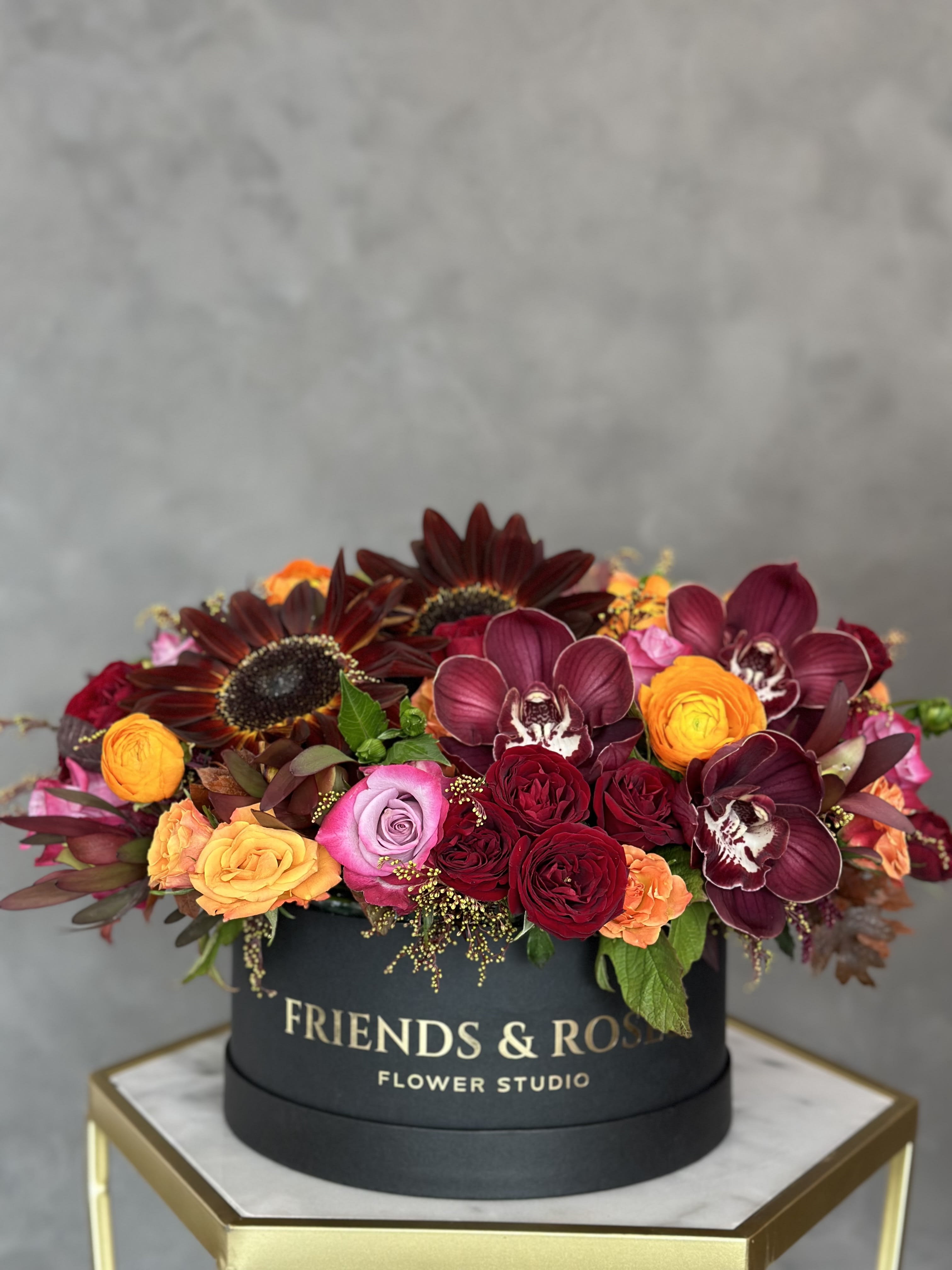 Round box arrangement with burgundy orchids, roses, and sunflowers