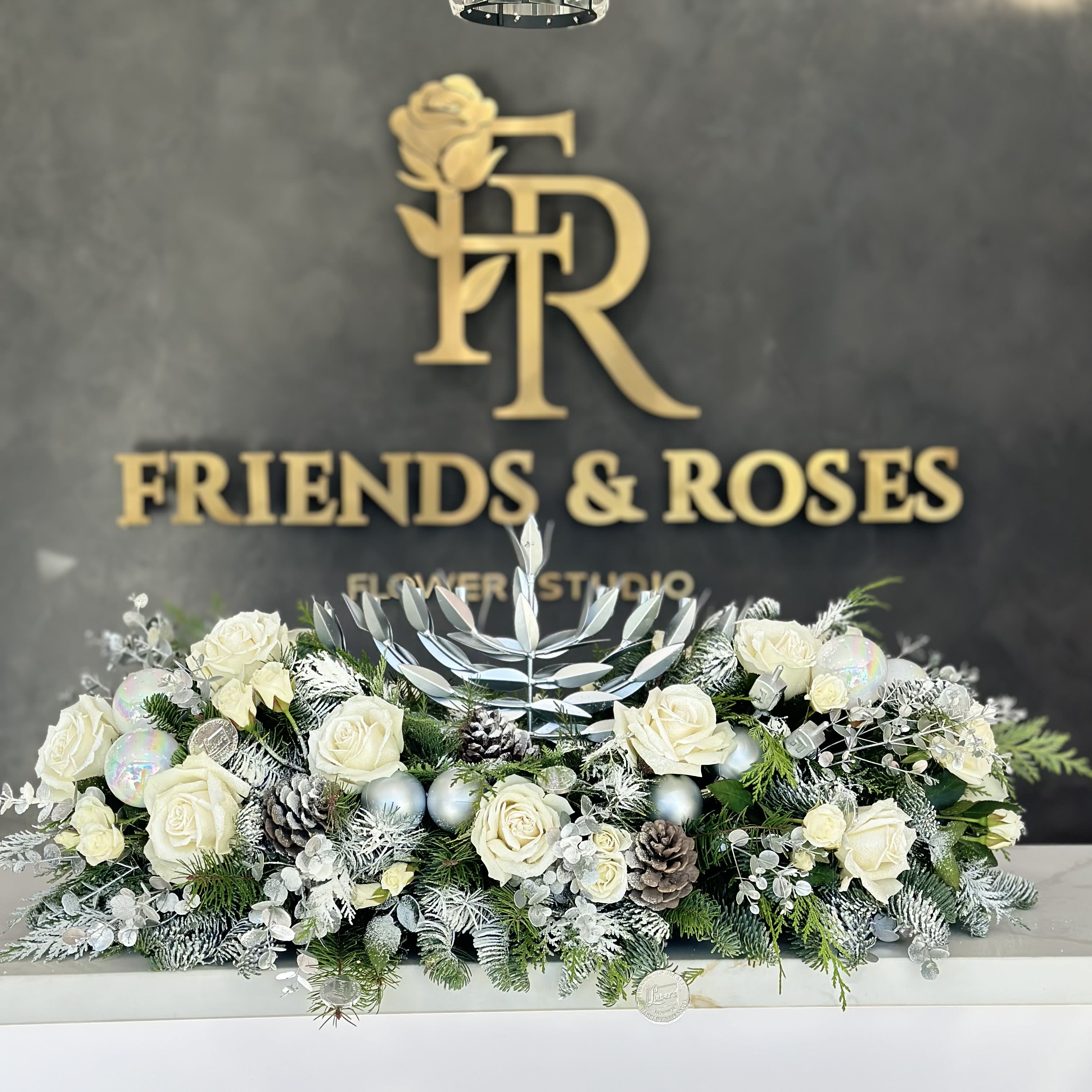 White roses arranged with frosted greenery and pinecones in a low centerpiece.