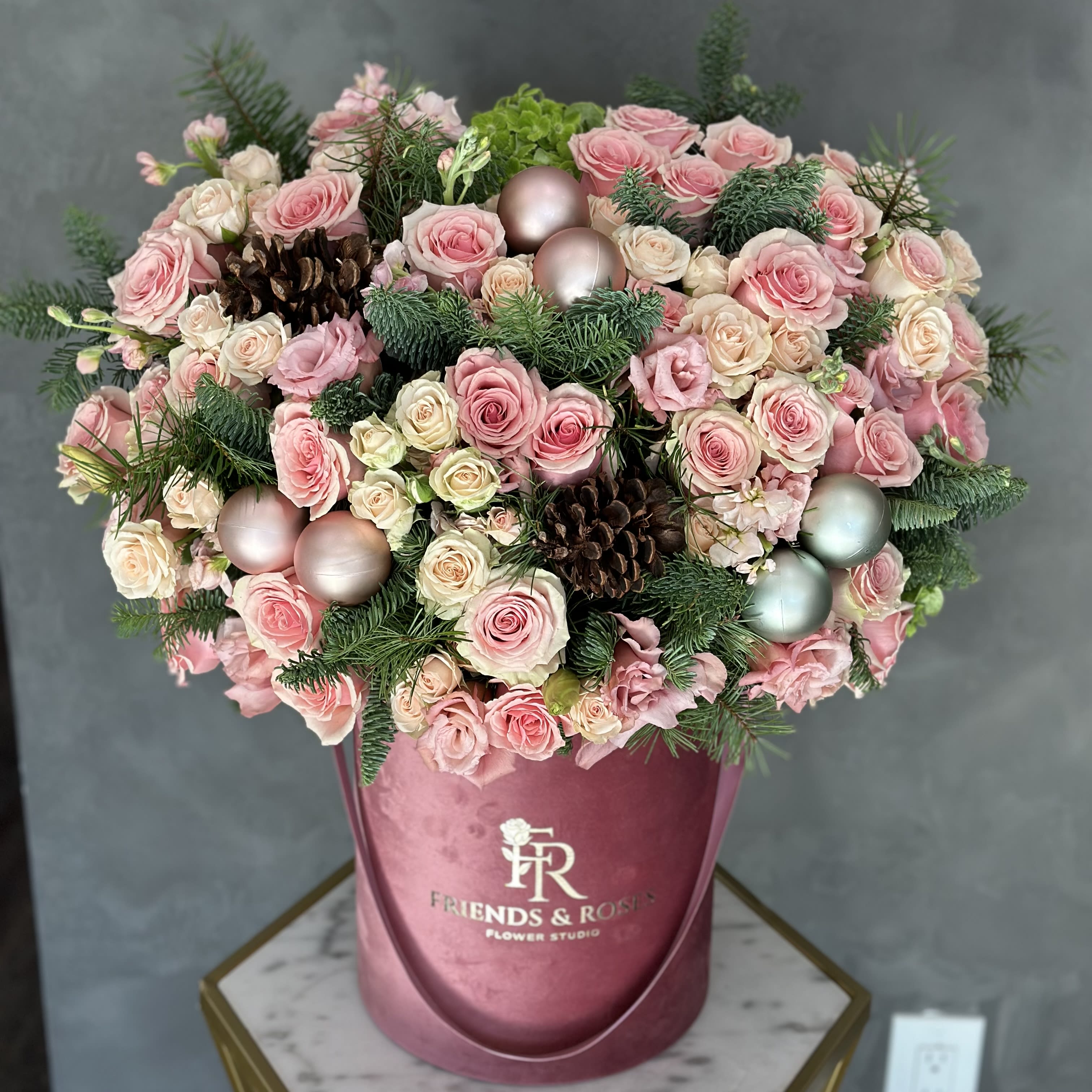 Pink and cream roses arranged in a round box with pinecones and ornaments