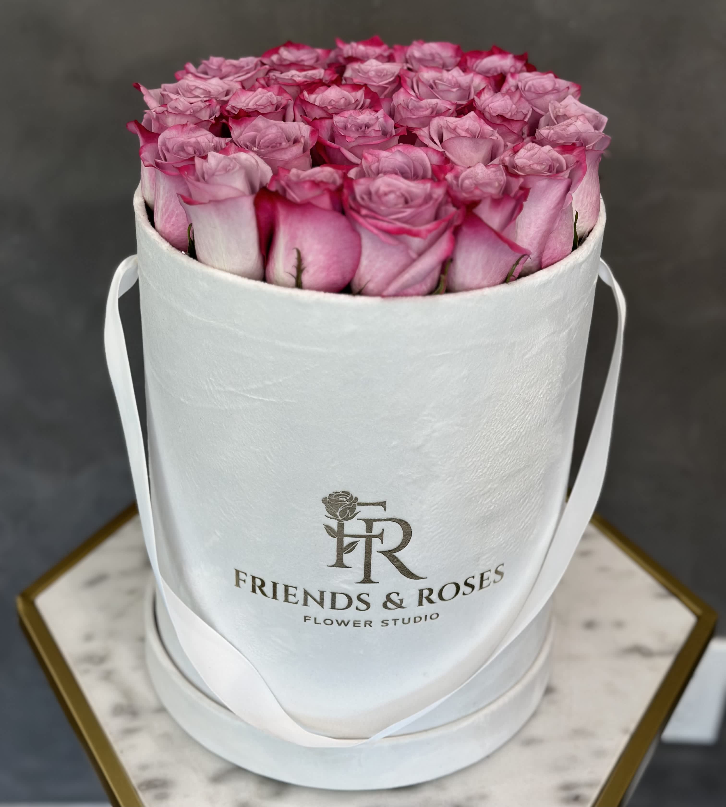 Pink roses arranged in a white round hat box with ribbon handles