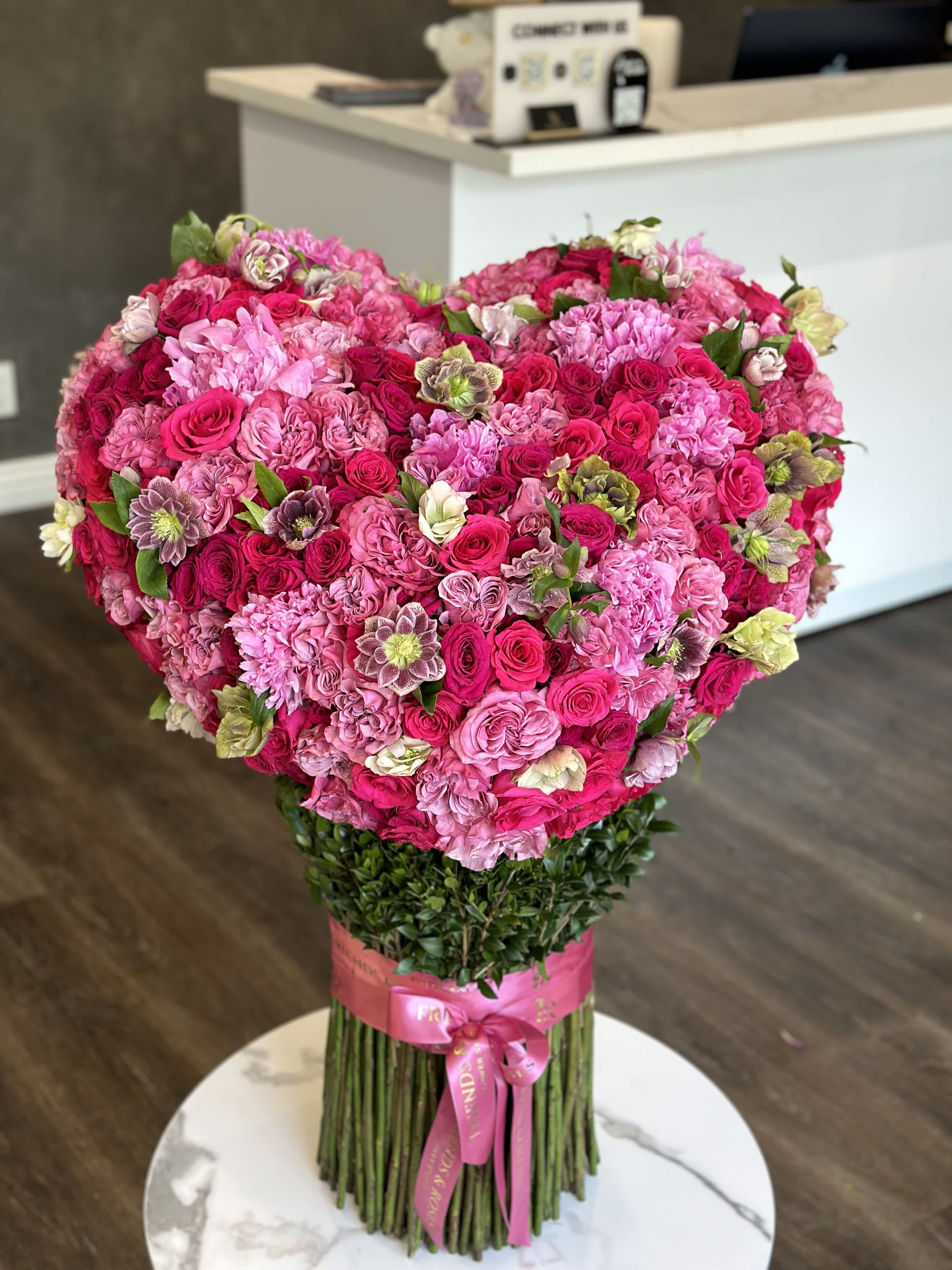 Large heart-shaped bouquet of pink and magenta roses with a ribbon-wrapped stem bundle