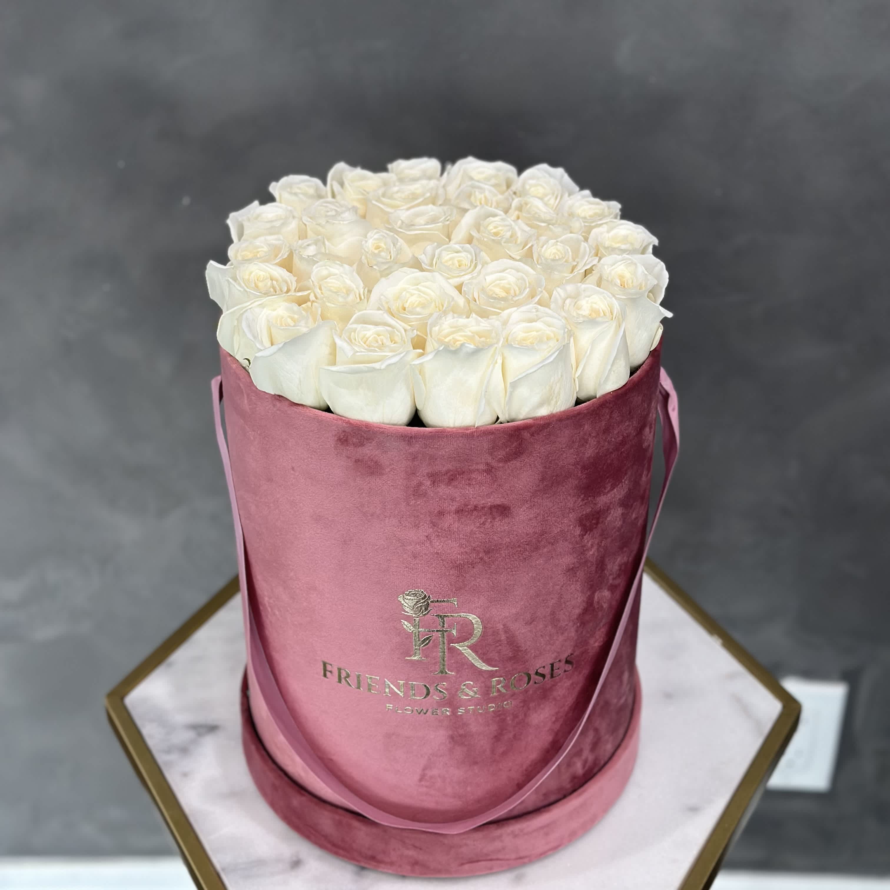 White roses arranged in a pink velvet hat box