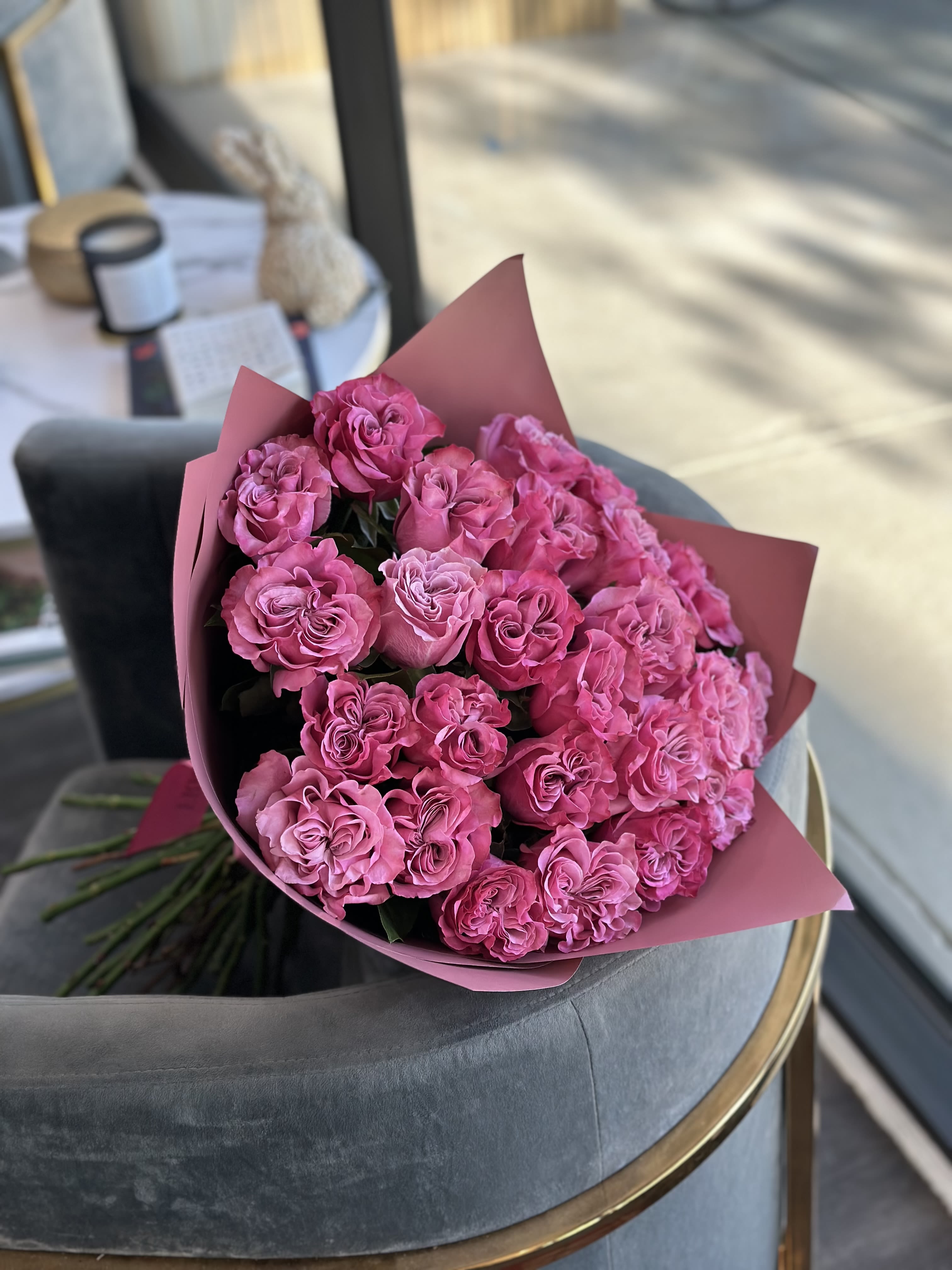 Large bouquet of bright pink roses wrapped in pink paper resting on a gray chair