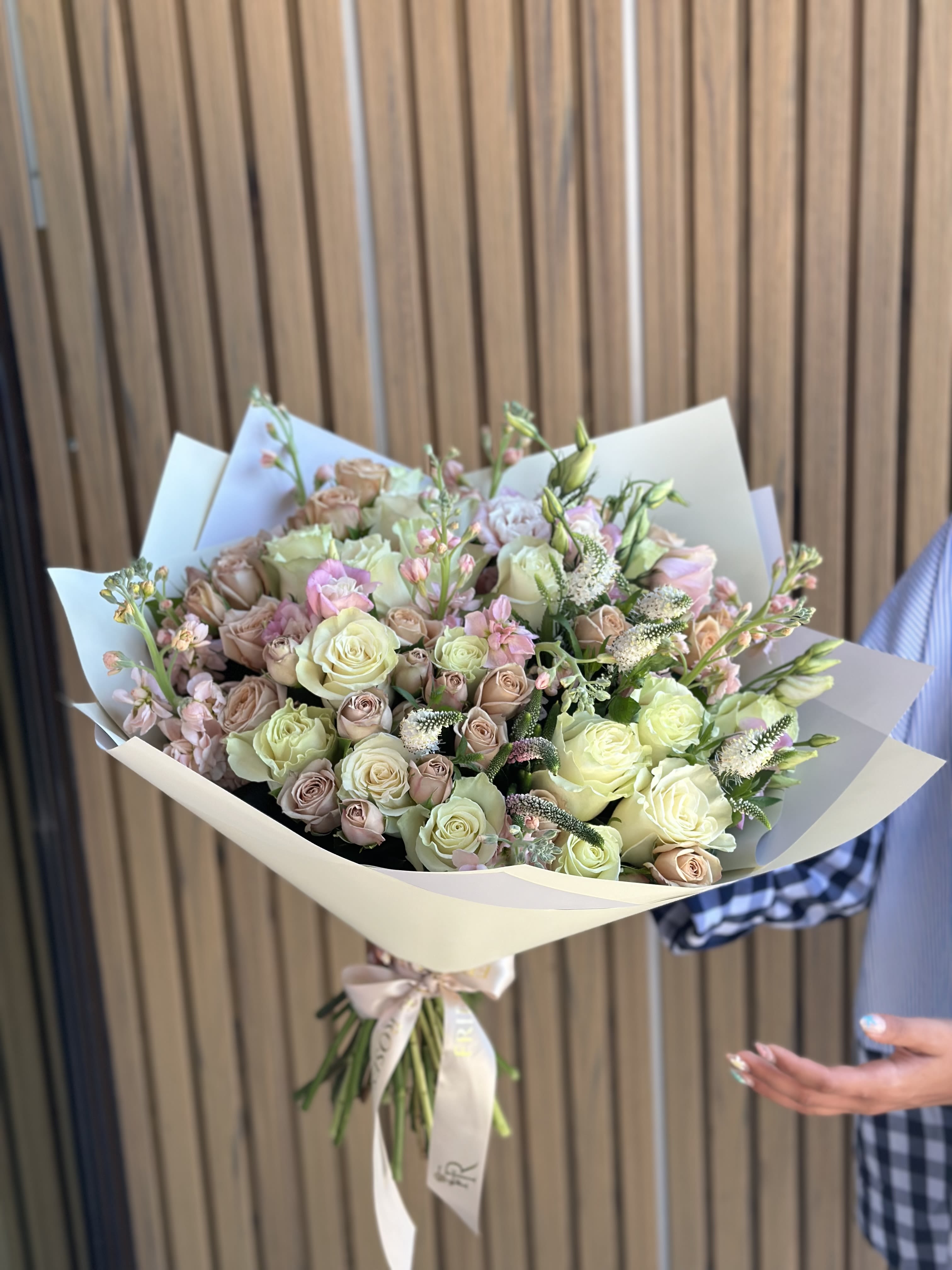 Bouquet of pale roses and pink filler flowers wrapped in cream paper