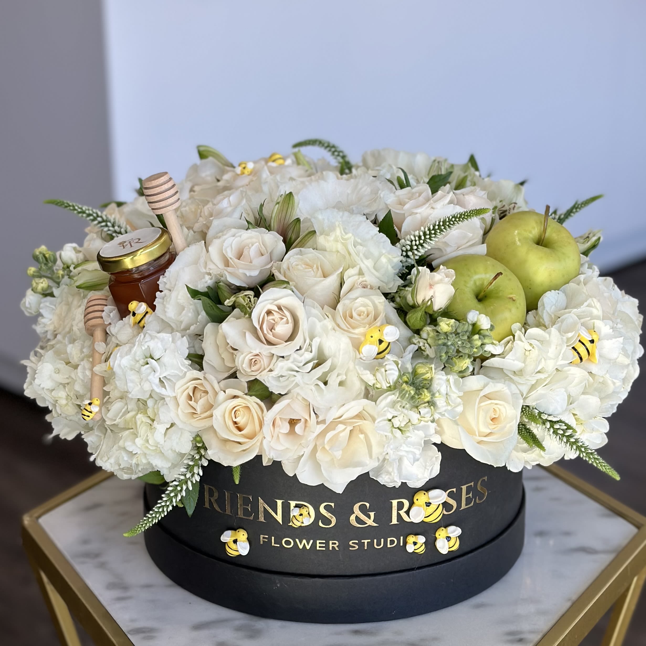 White roses and hydrangeas in a black hat box with green apples and honey jars