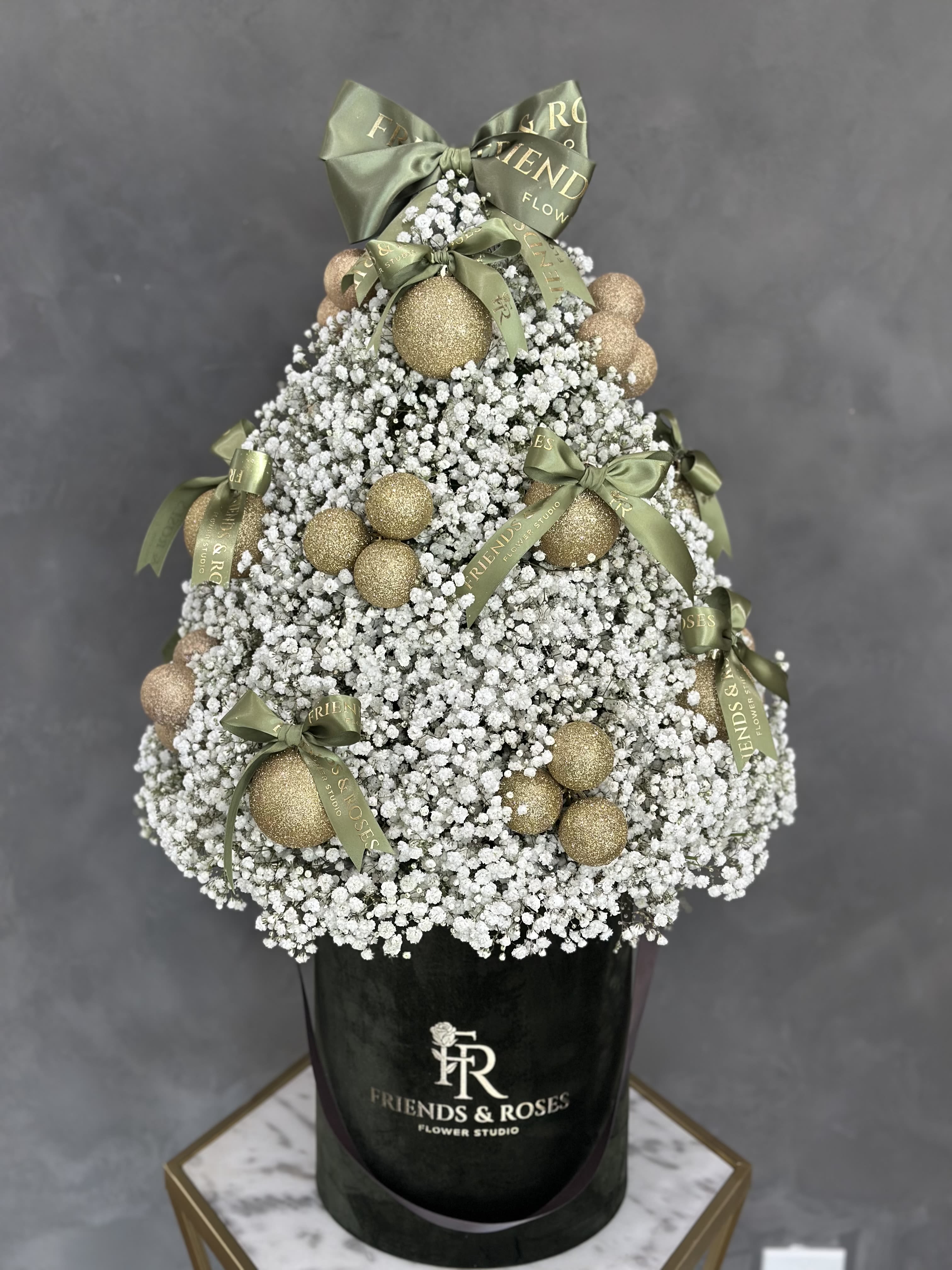 White baby's breath arrangement with gold ornaments and green bows in a black box