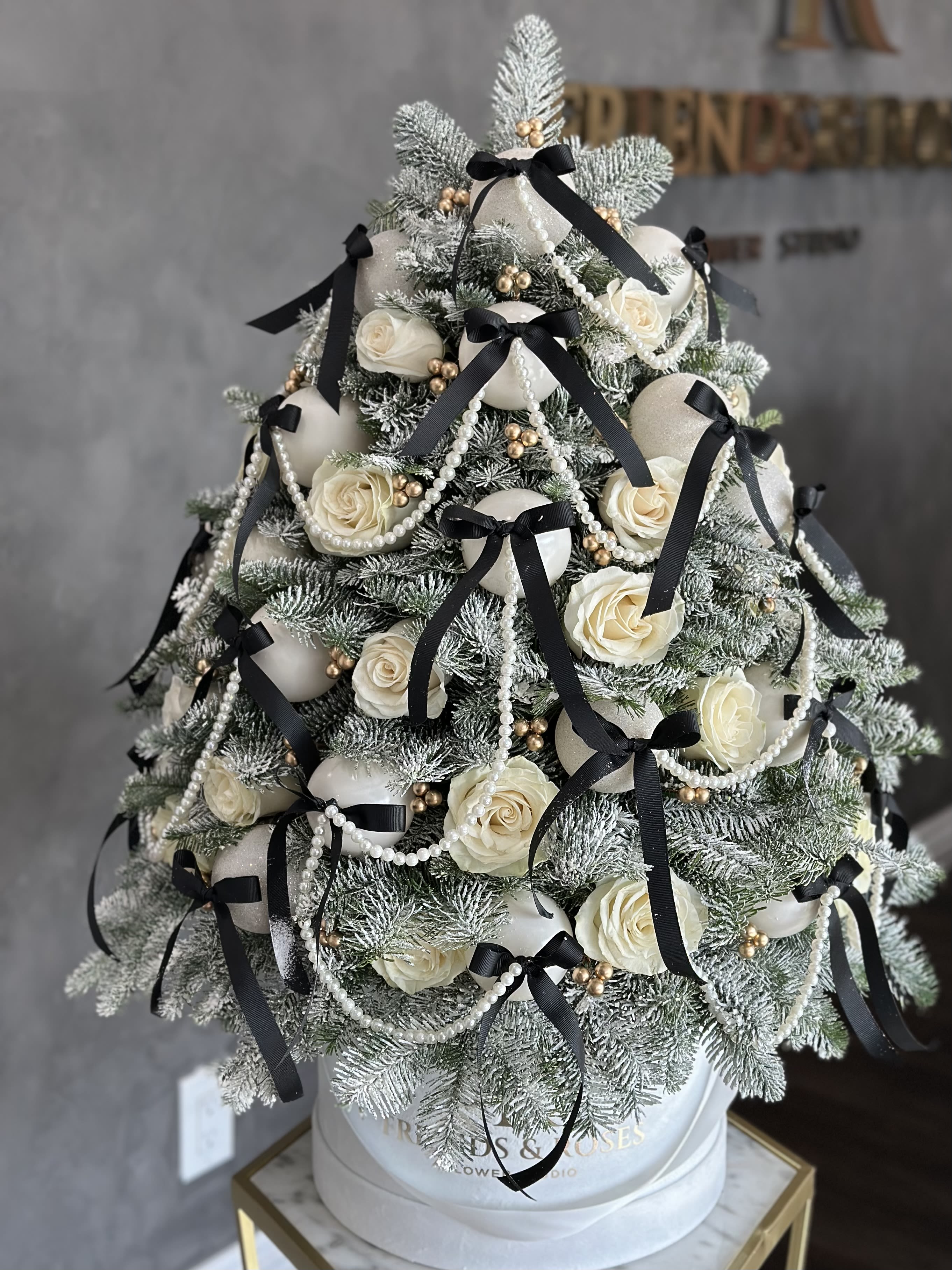 Snow-dusted evergreen tree with white roses, black ribbons, and pearl garlands