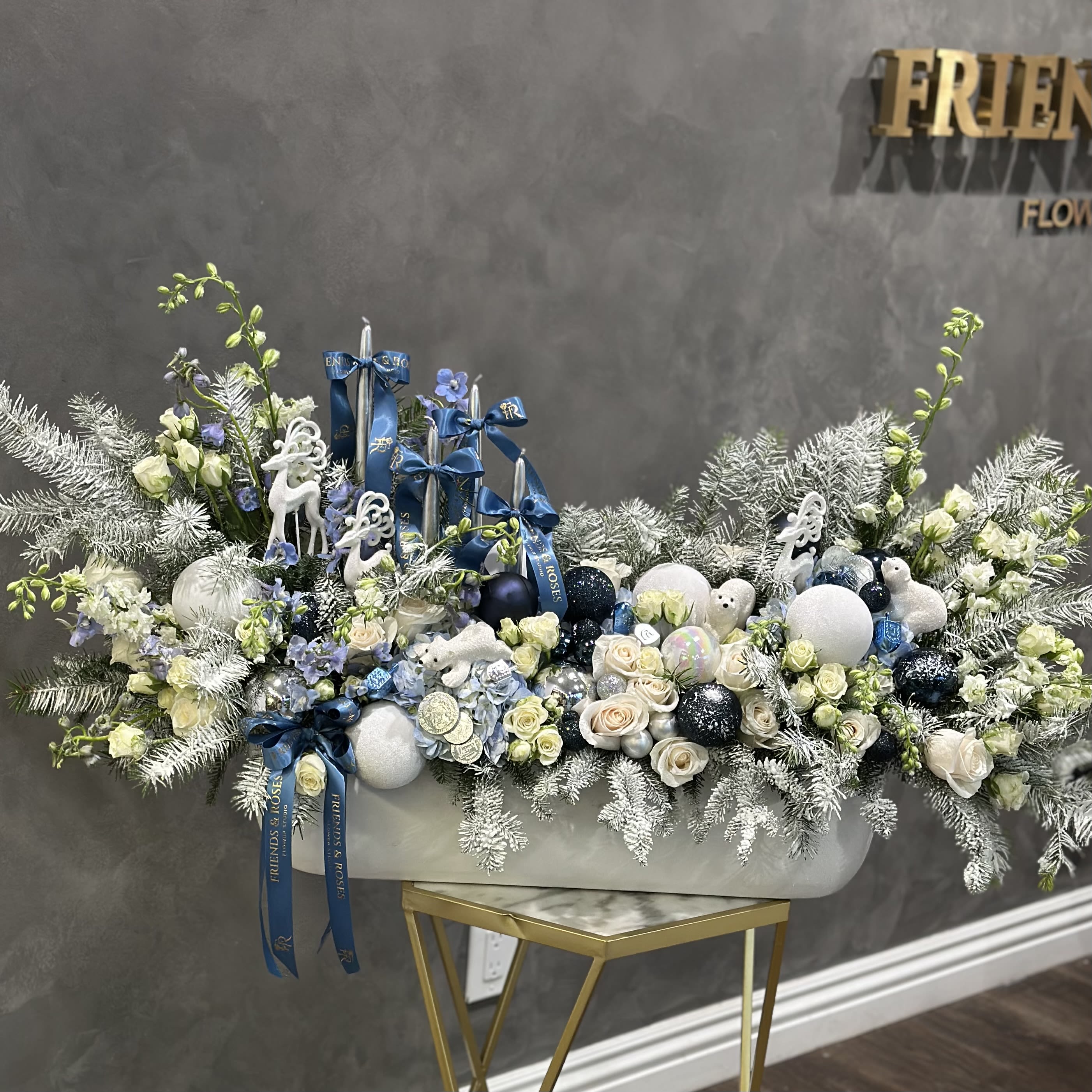 Large white floral arrangement with blue ribbons and ornaments in a white container