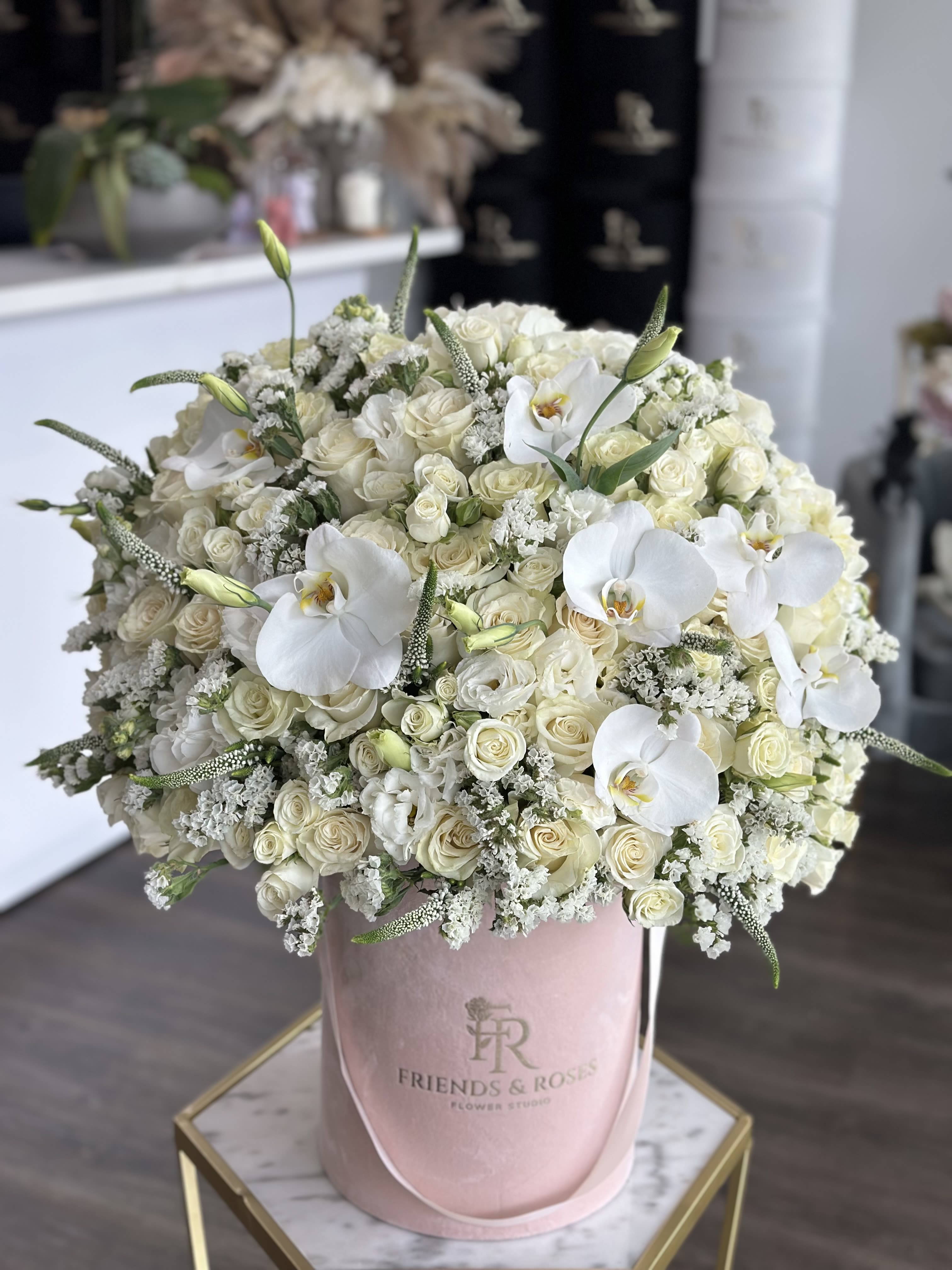 Large white rose and orchid arrangement in a pink hatbox
