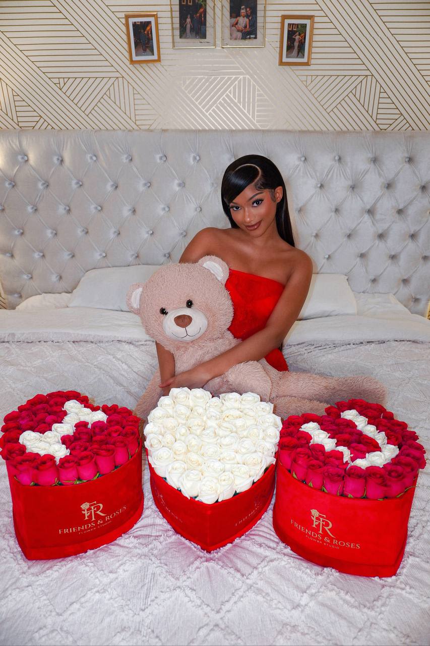 Woman holding a teddy bear with three heart-shaped rose boxes on a bed