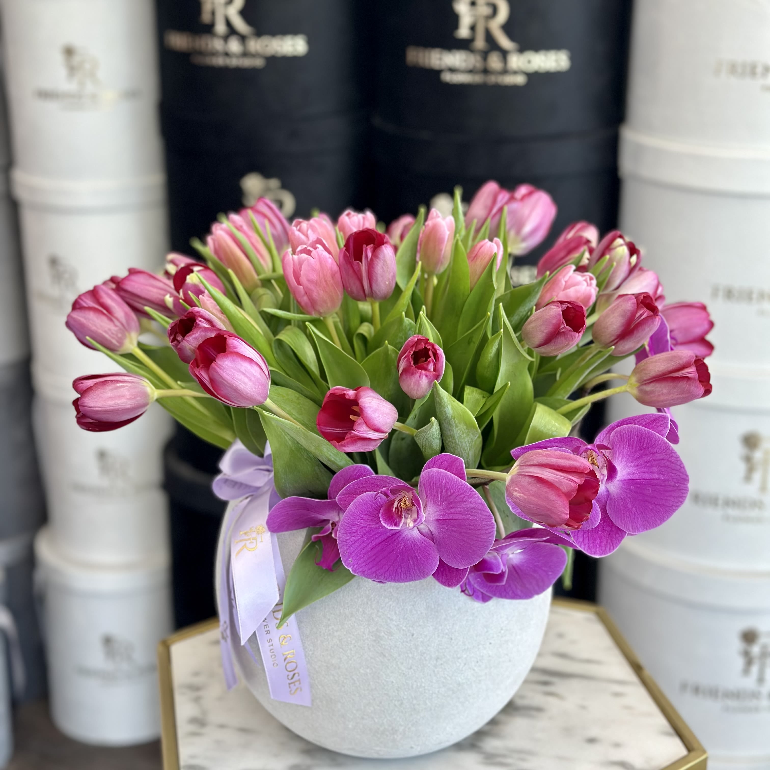 Pink tulips and purple orchids arranged in a round white vase