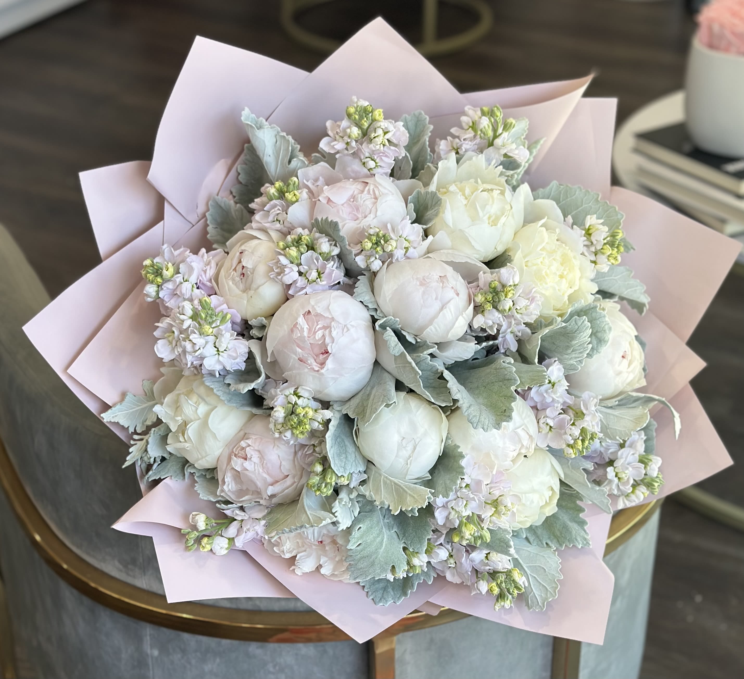 Bouquet of pale peonies and small lavender flowers wrapped in pink paper