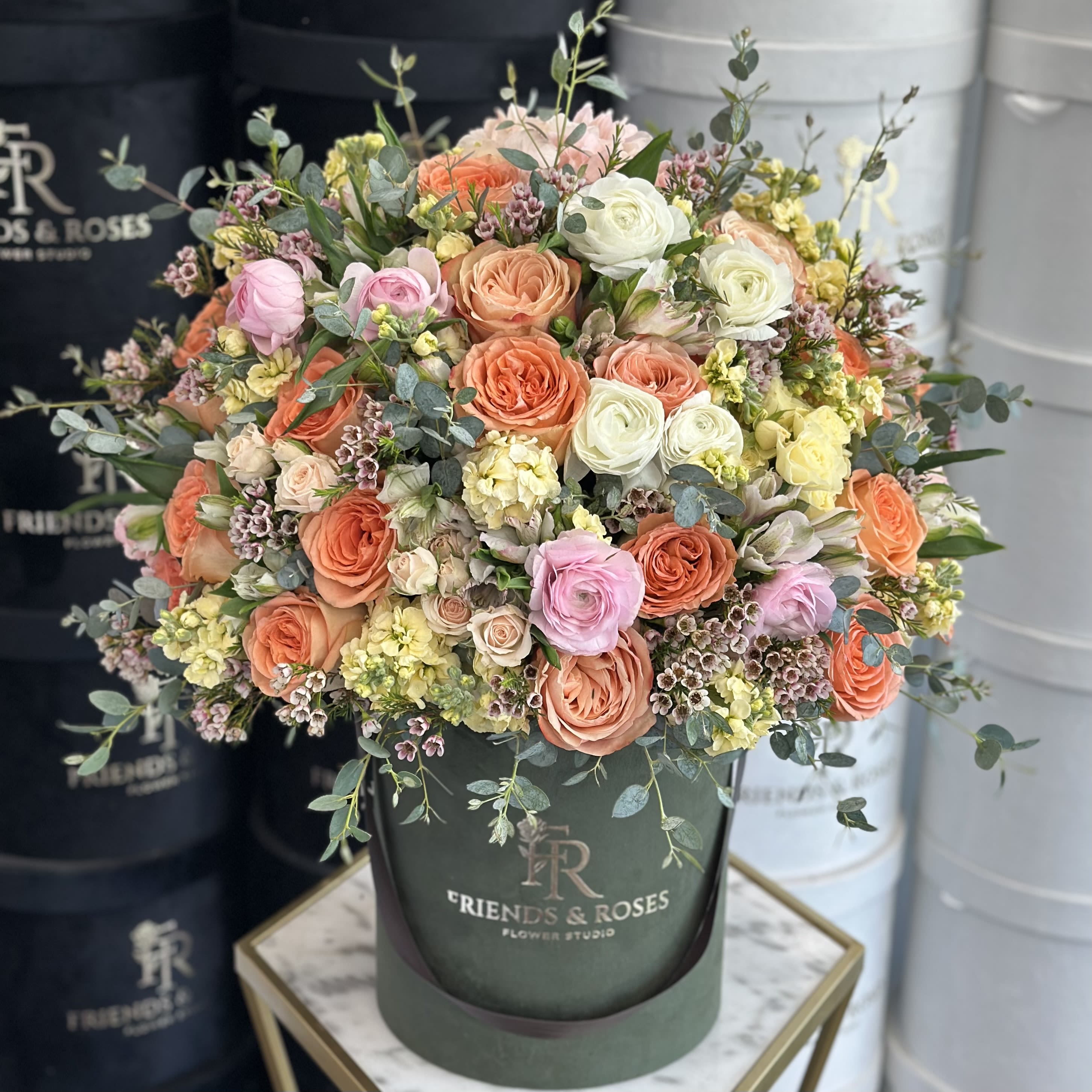 Mixed pastel roses and small filler flowers in a dark green hatbox