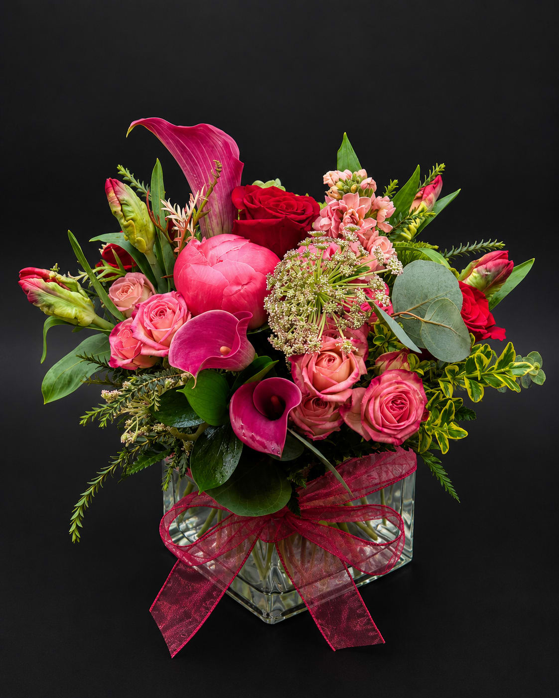 Pink and red floral arrangement in a clear glass vase with a ribbon