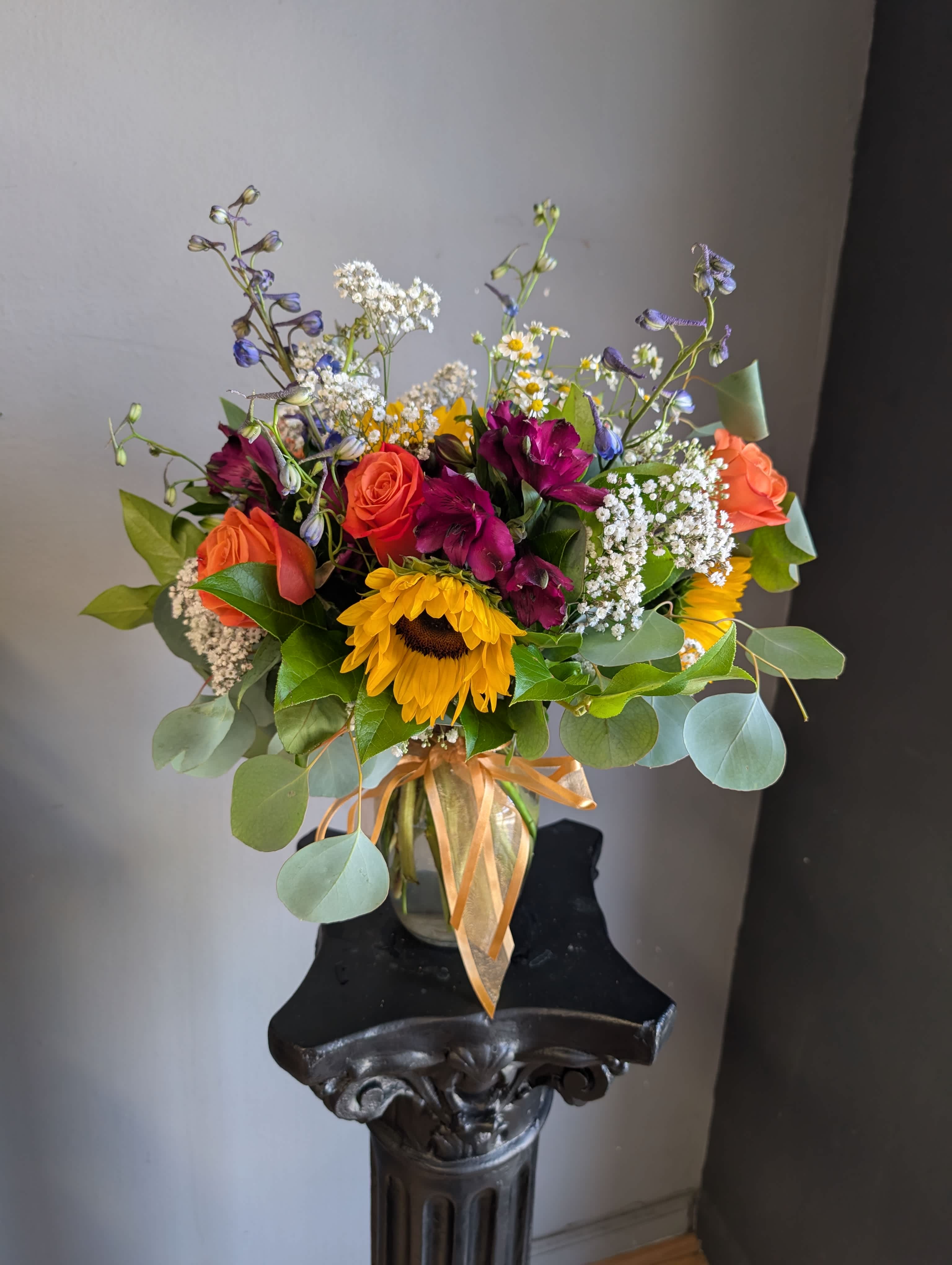 Mixed bouquet with sunflowers, roses, and purple blooms in a glass vase