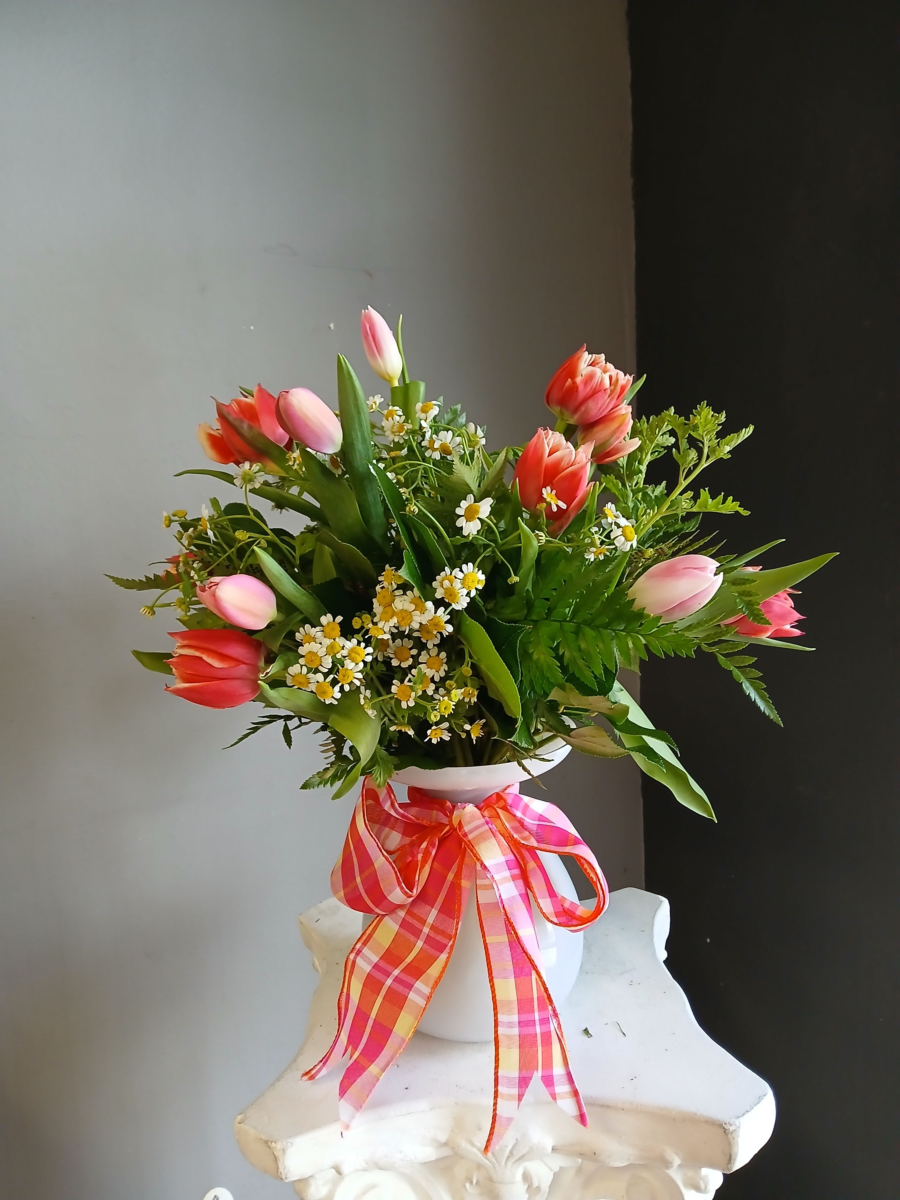 Pink and coral tulips arranged in a white vase with a plaid ribbon