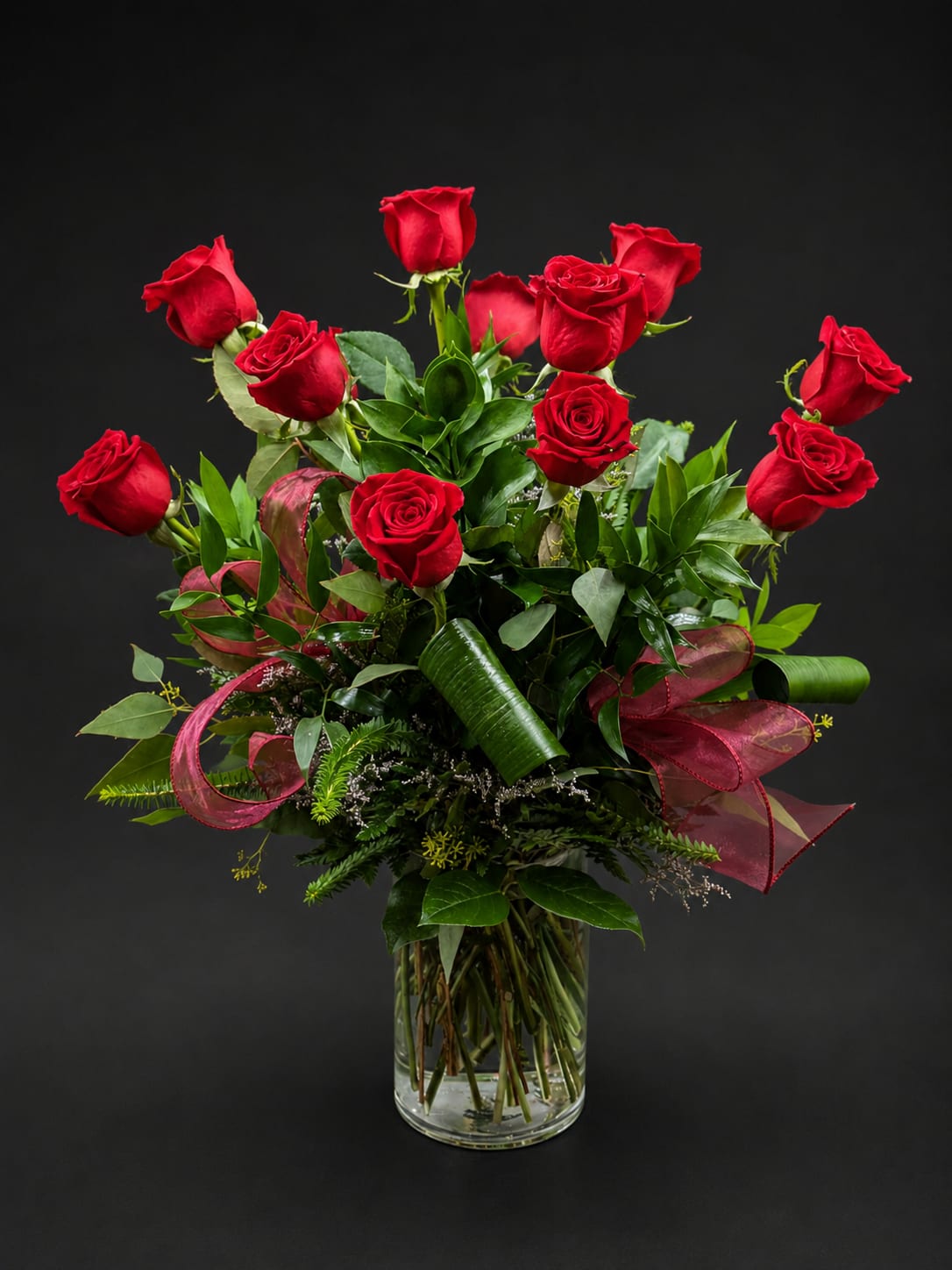 Red roses arranged in a clear glass vase with ribbon accents