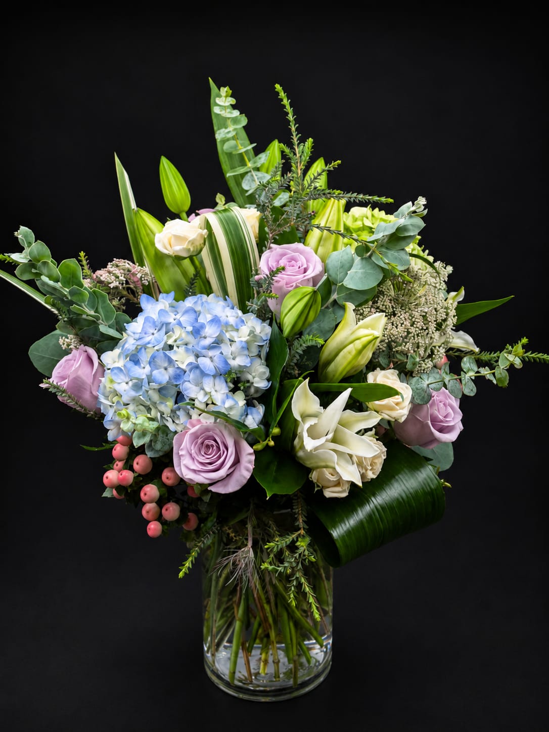 Mixed bouquet of pastel roses, hydrangea, and lilies in a glass vase