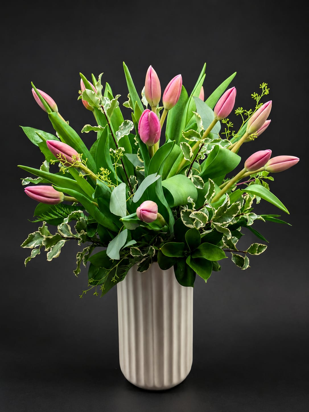 Pink tulips arranged in a tall white vase with mixed greenery