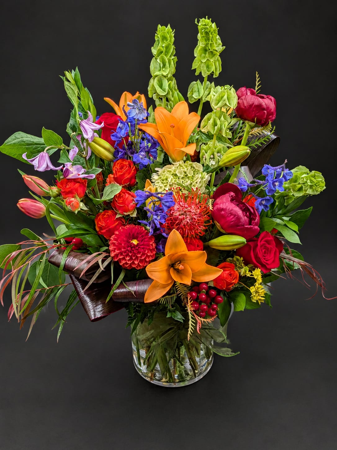 Colorful mixed bouquet in a clear glass vase with lilies, roses, and peonies