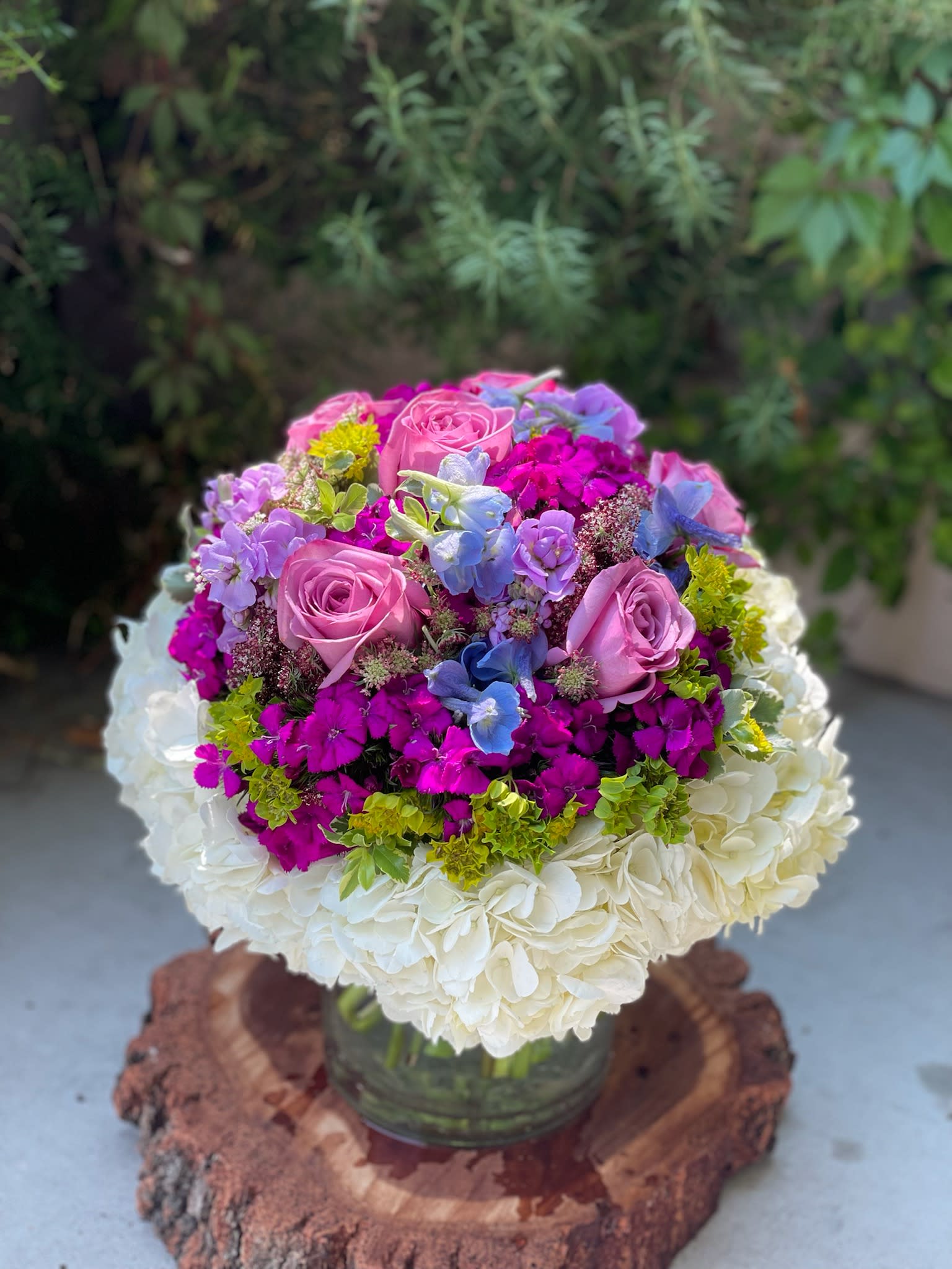 Round bouquet of pink roses, hydrangeas, and purple flowers in a glass vase