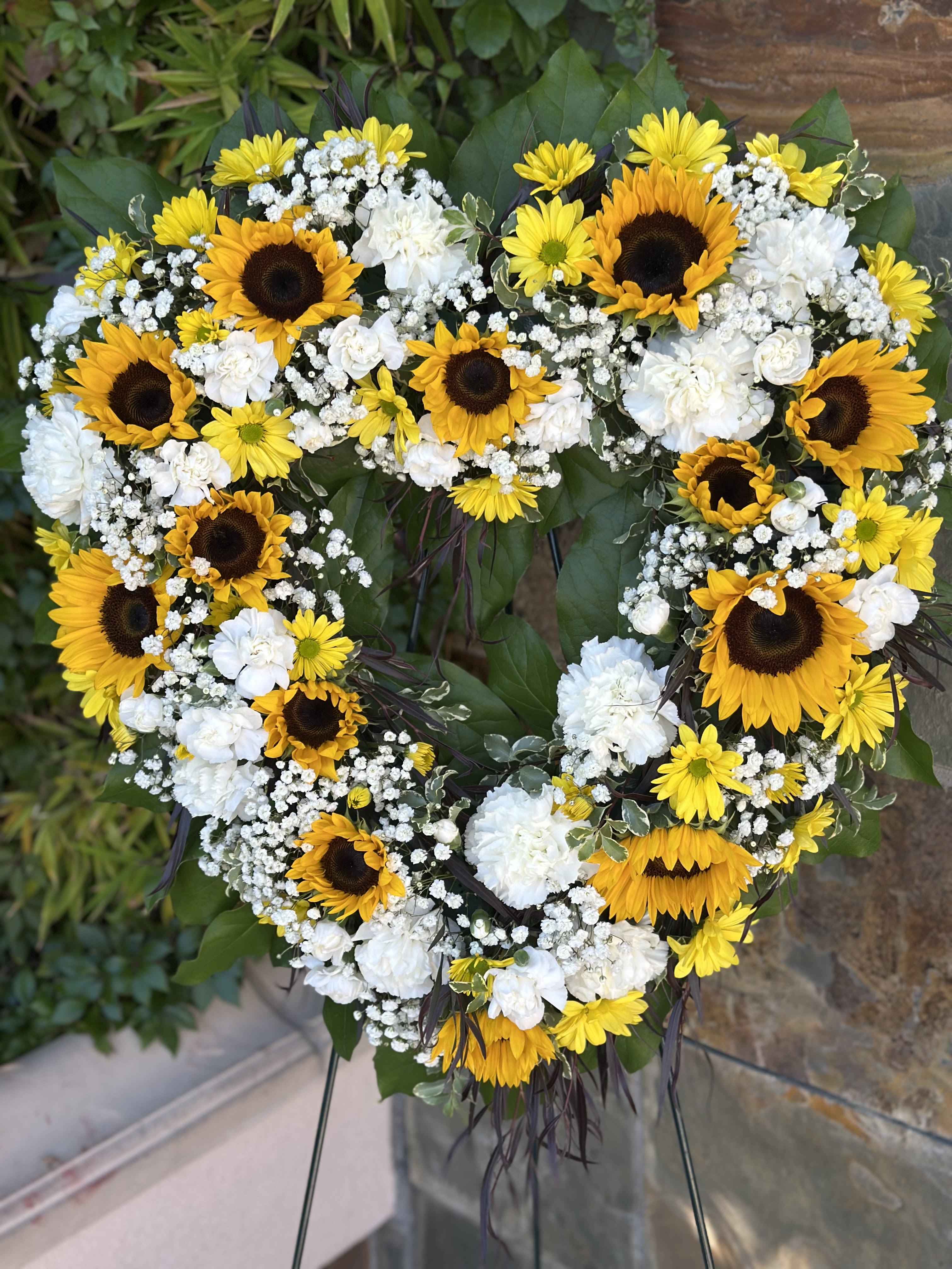 Heavenly Sunshine - A bright funeral open heart with sunflowers, daisies and carnations on a 48" easel.