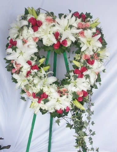 Heart-shaped floral wreath with white lilies and pink roses on a stand