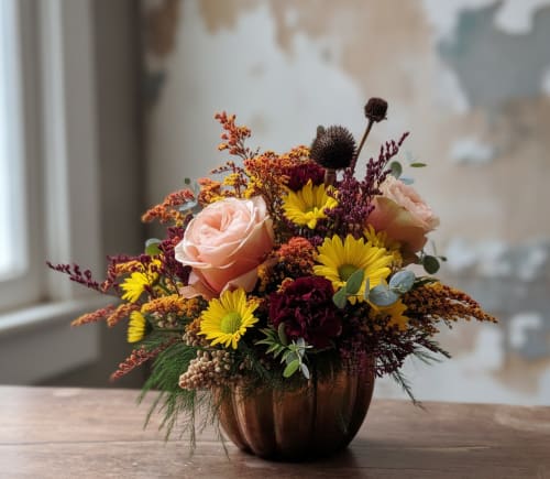 Mixed bouquet of roses and yellow daisies in a copper pumpkin vase