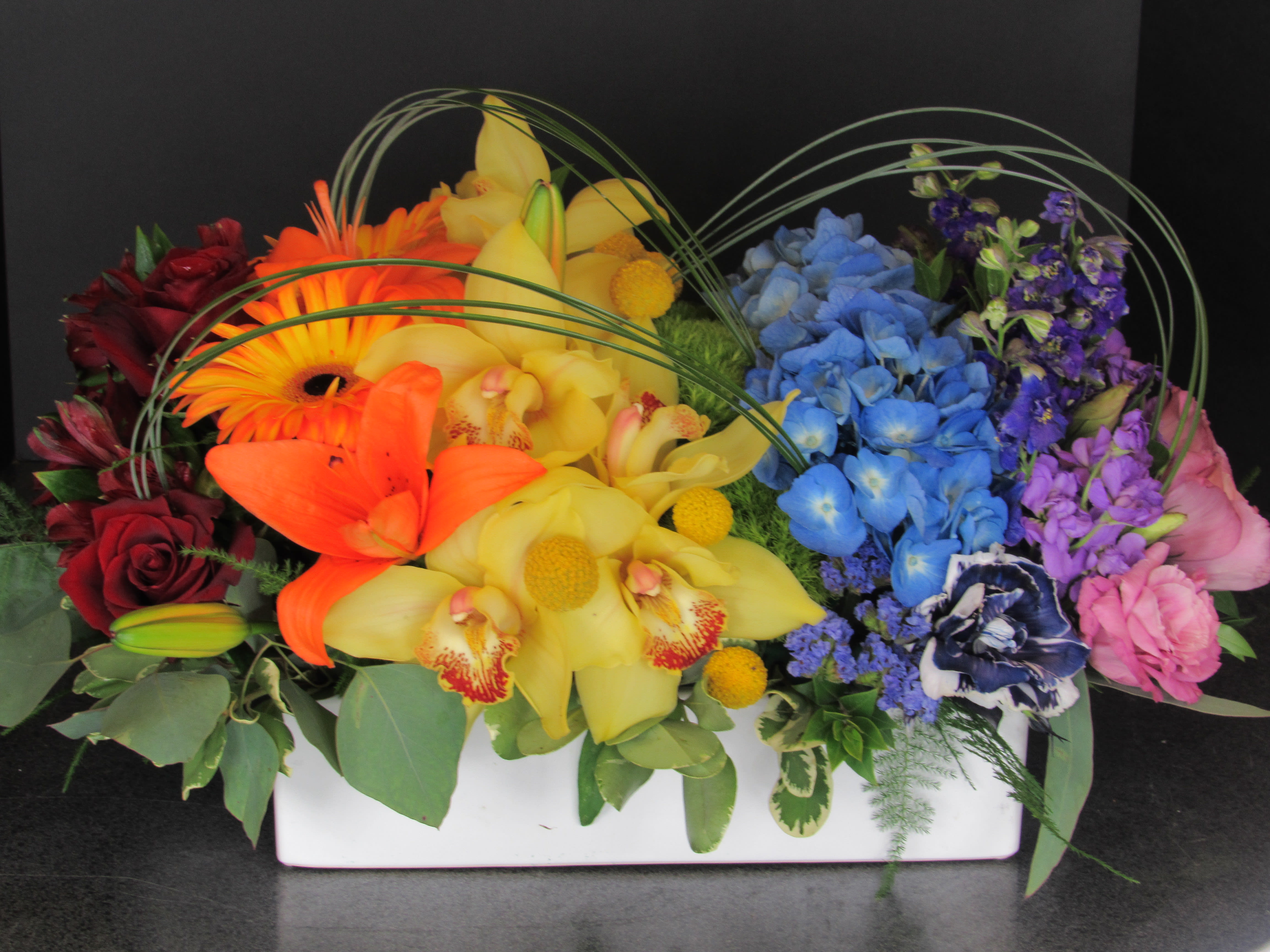 Rainbow Garden - Roses, Lilies, Hydrangea, Orchids and other spring flowers designed in all the colors of the rainbow! Perfect gift to show your pride or to brighten someone's day. Arranged in ceramic low-dish. Arrangement is 18"LX12"Wx10"H