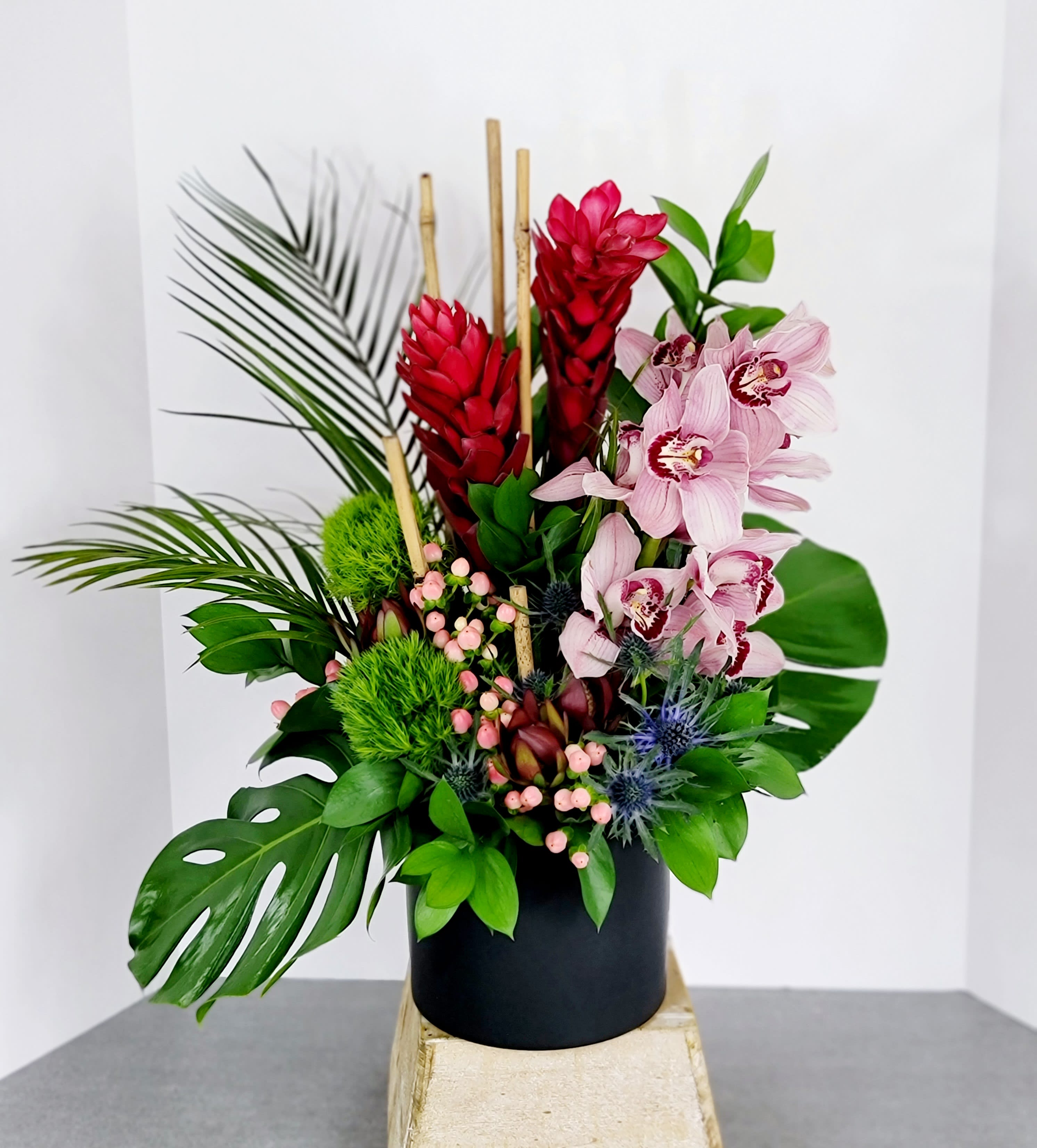 Tropical arrangement with pink orchids and red ginger in a black vase