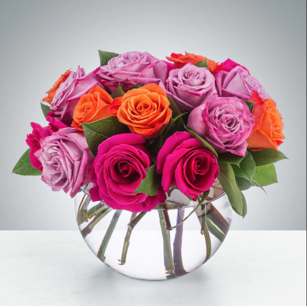 Mixed pink, lavender, and orange roses in a clear round vase