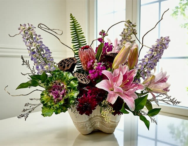 Mixed bouquet with pink lilies and purple flowers in a cream vase