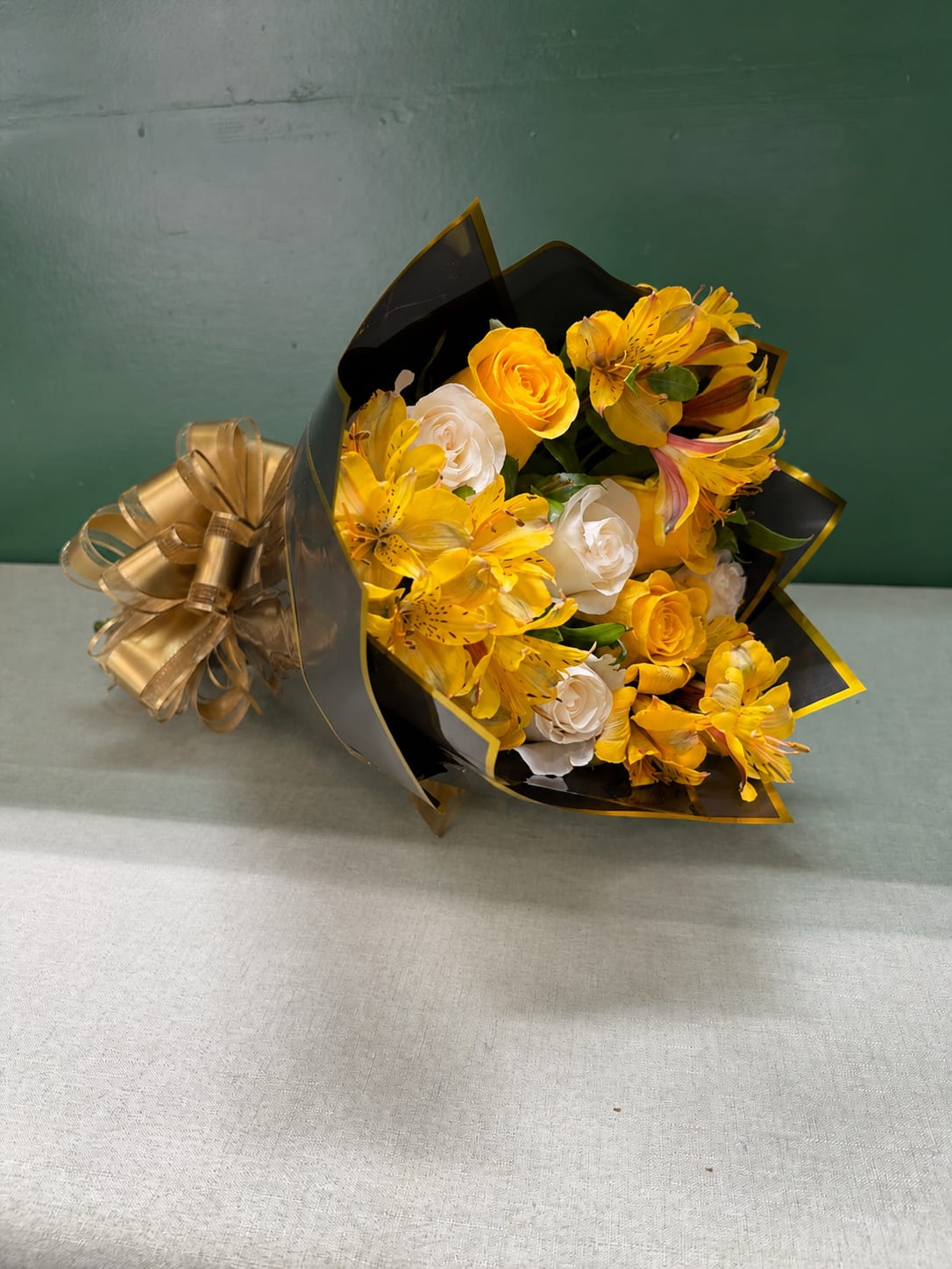 Yellow and white bouquet wrapped in black paper with a gold ribbon