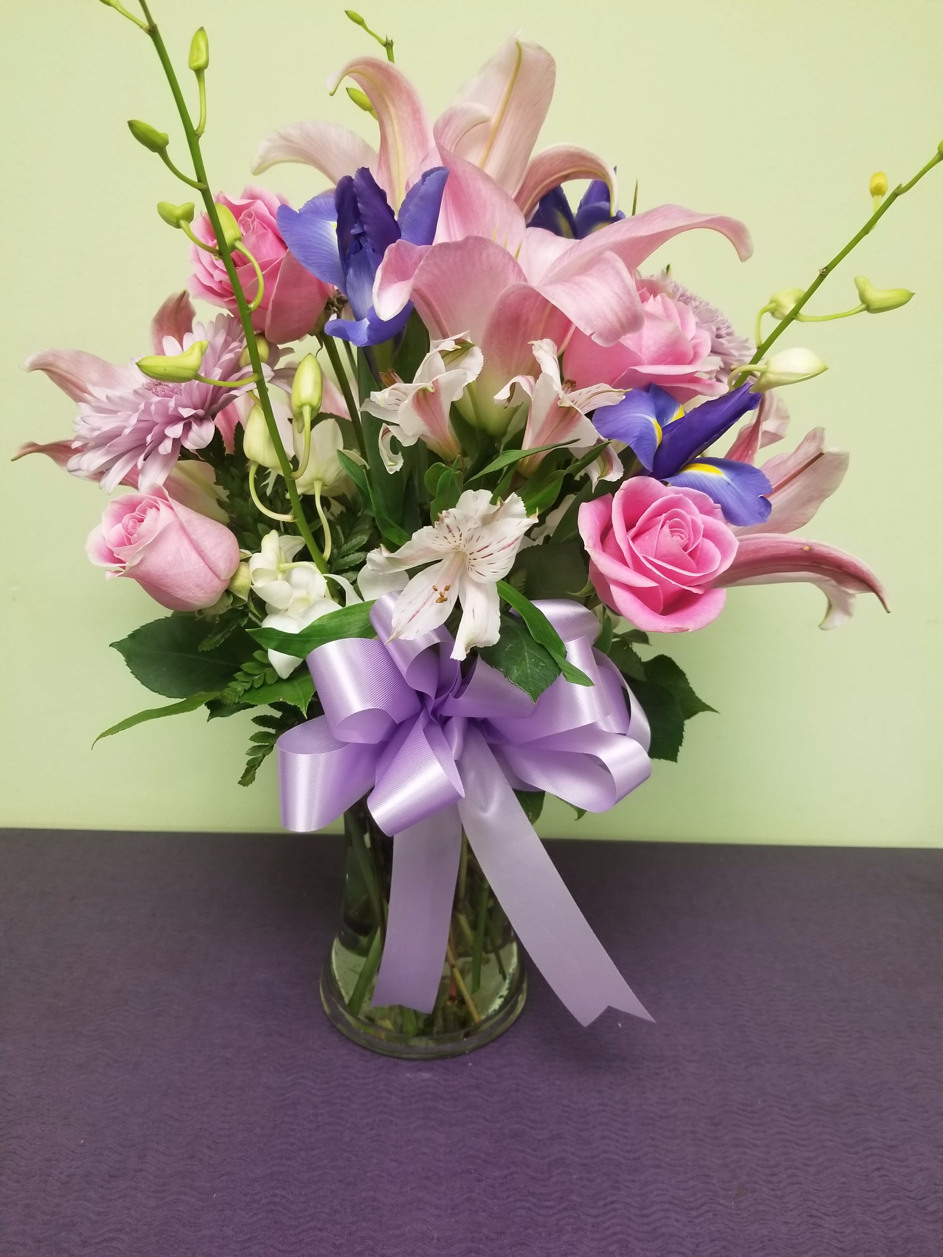Pink and purple mixed bouquet in a glass vase with a lavender ribbon