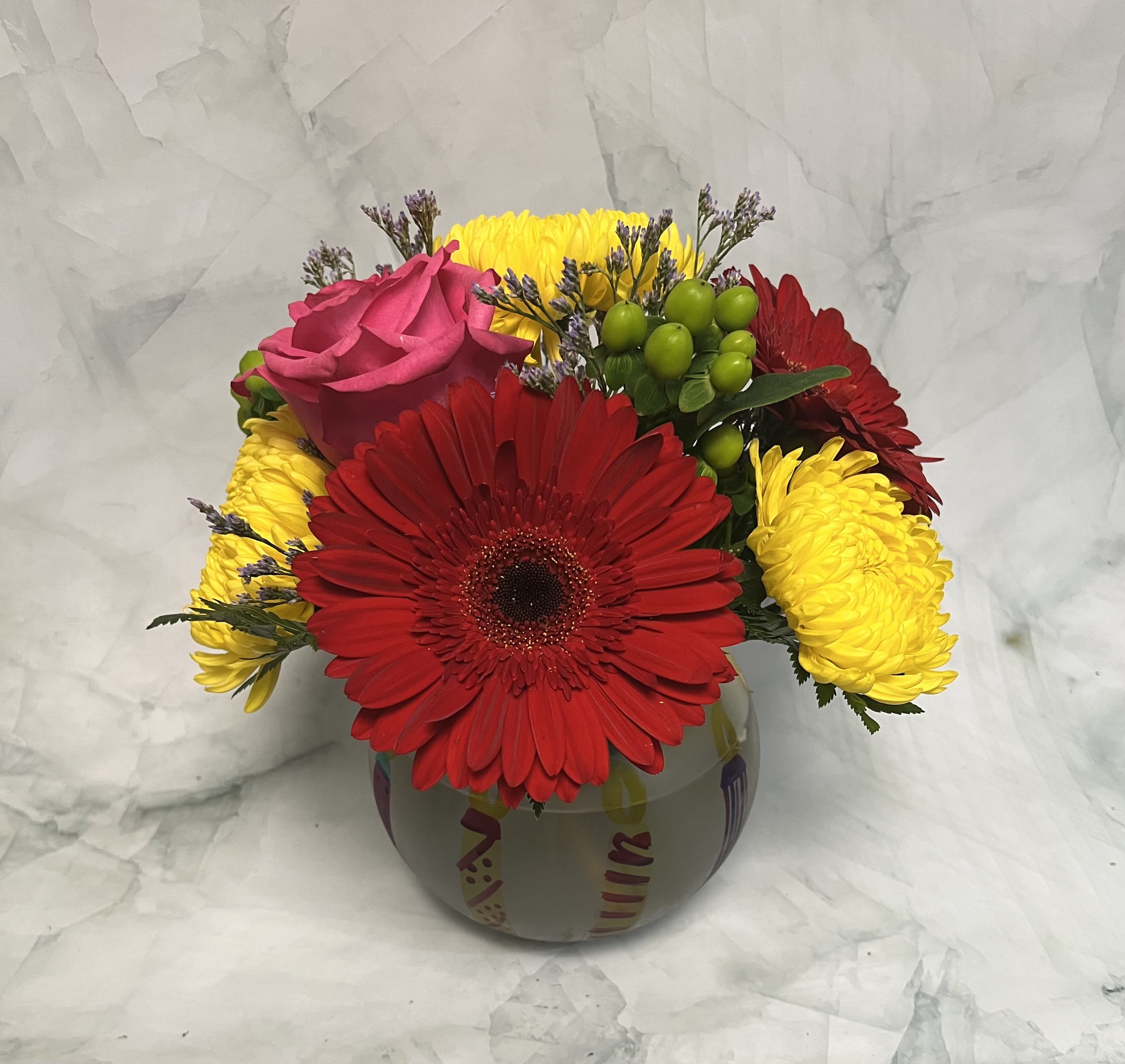 Bouquet of red gerbera daisies, yellow mums, and a pink rose in a round vase