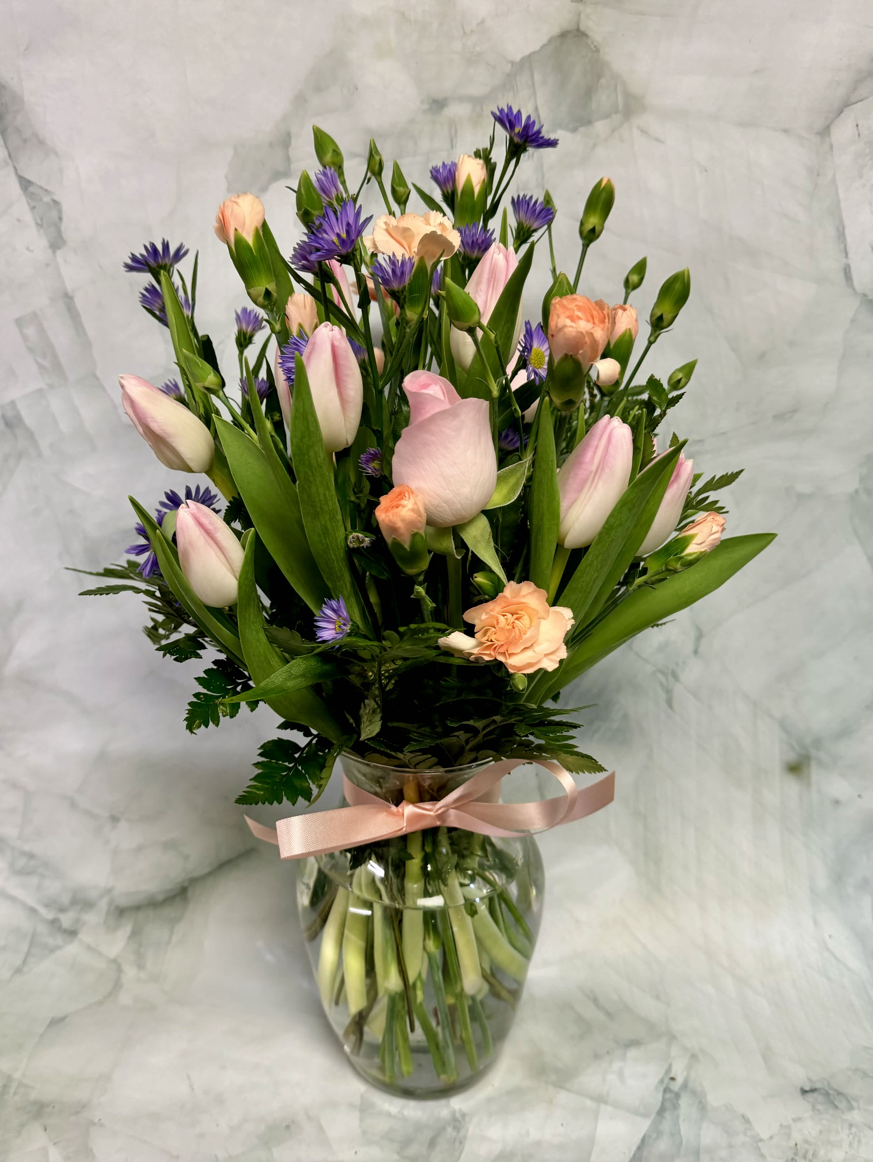 Pink tulips and peach carnations in a glass vase with a ribbon