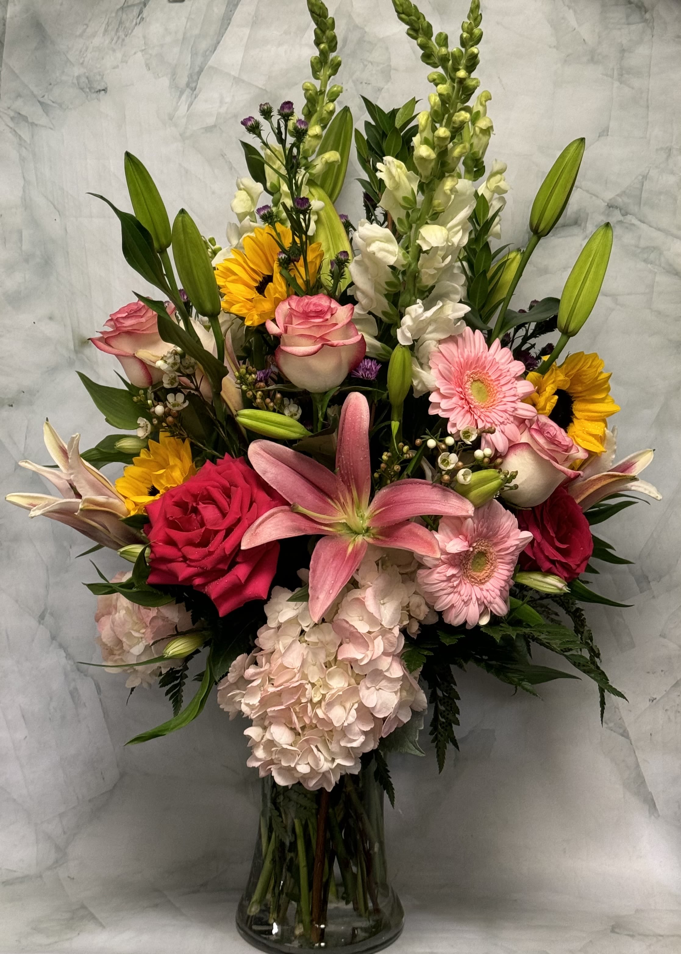 Mixed bouquet with pink roses, lilies, gerberas, sunflowers, and hydrangea in a glass vase